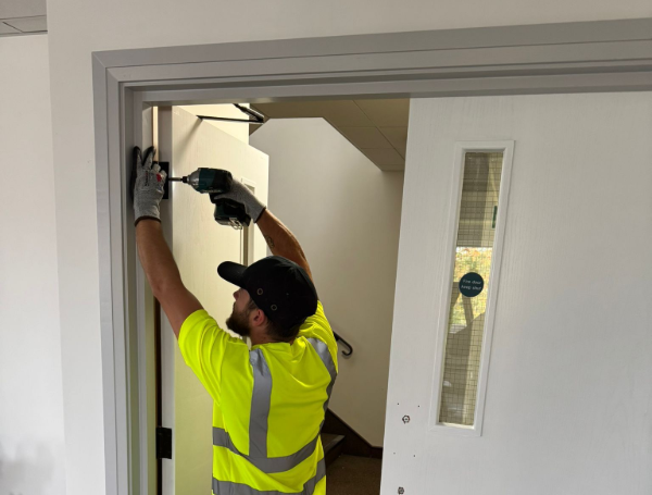 Person in safety vest using a drill to install hardware on a door frame.