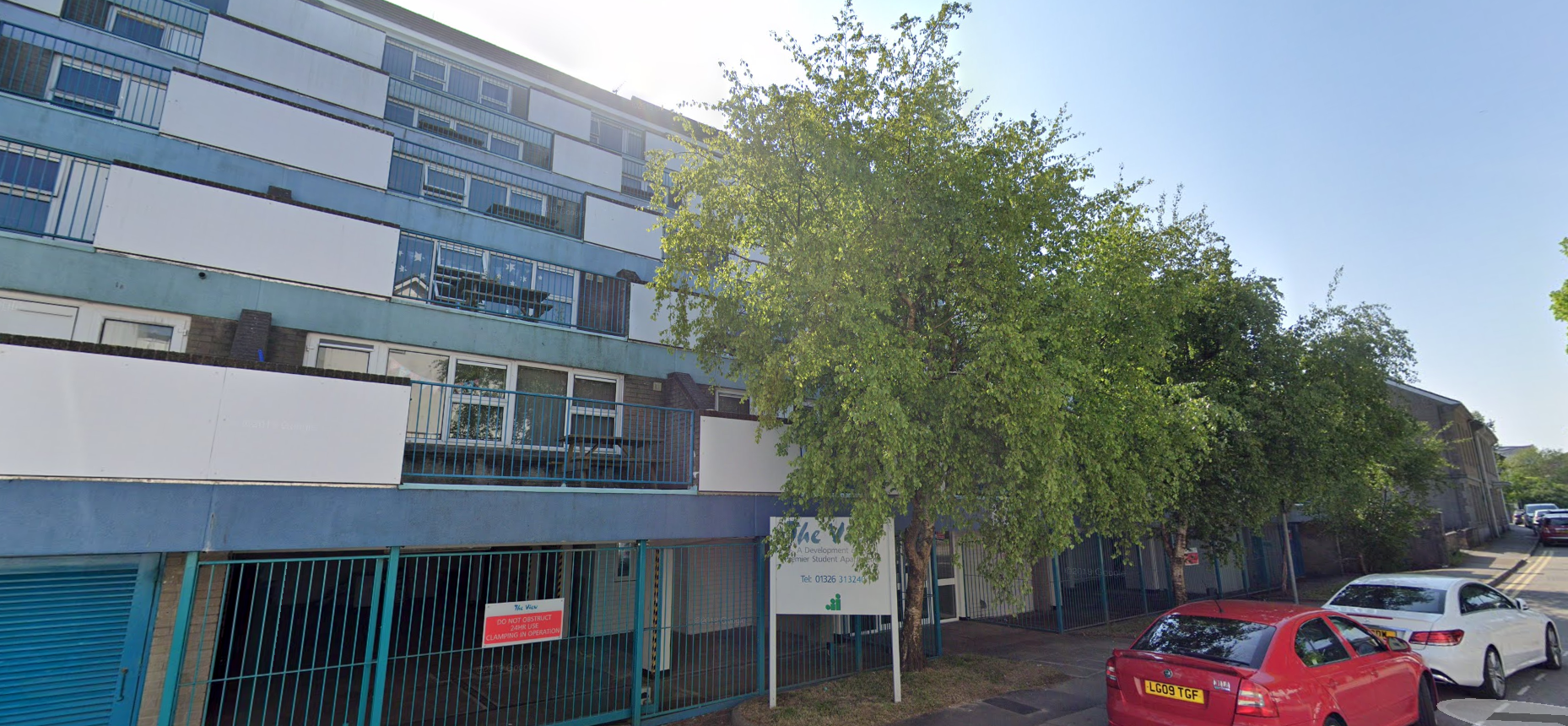 A multi-story blue building with trees in front and cars parked on a road.