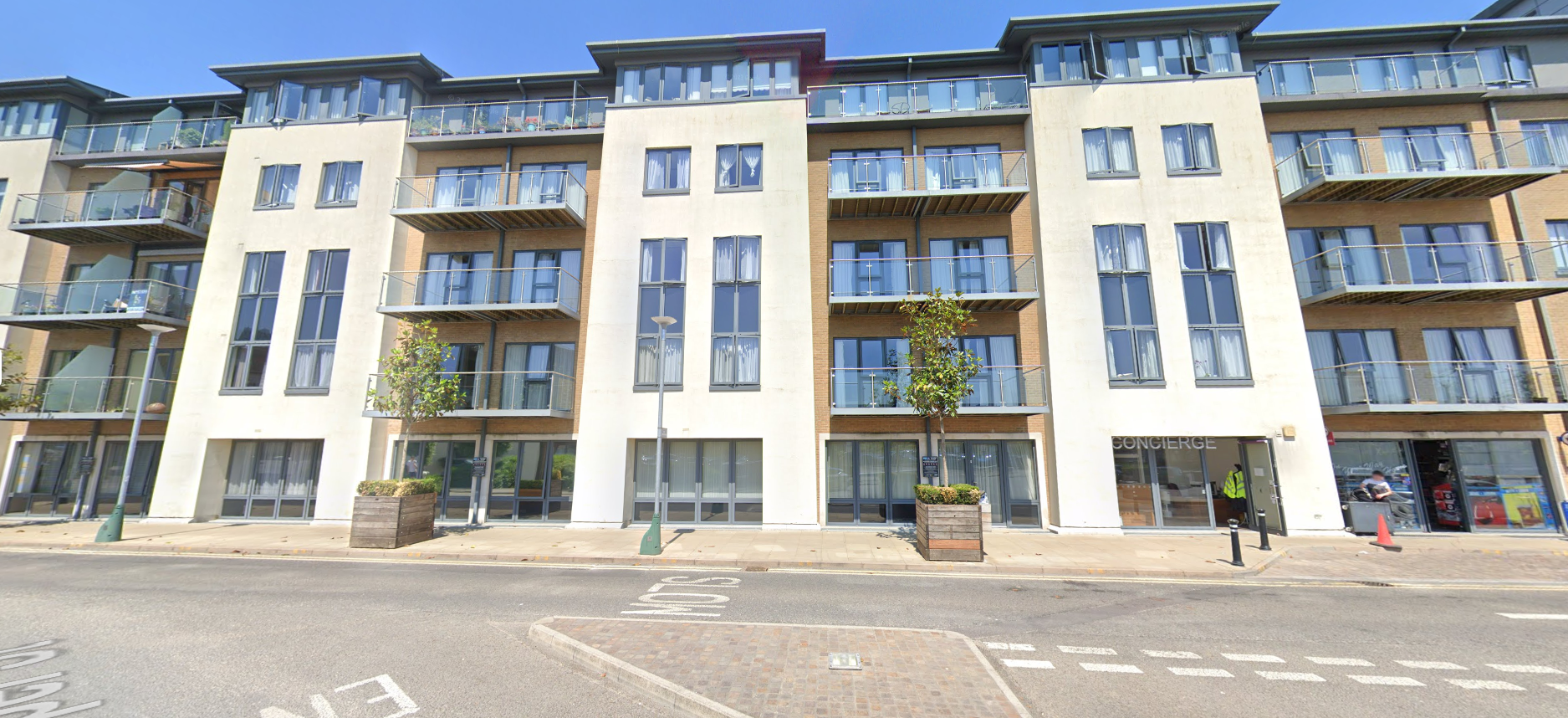 Multi-story apartment building with balconies and glass railings. Street level with storefronts and sidewalk.