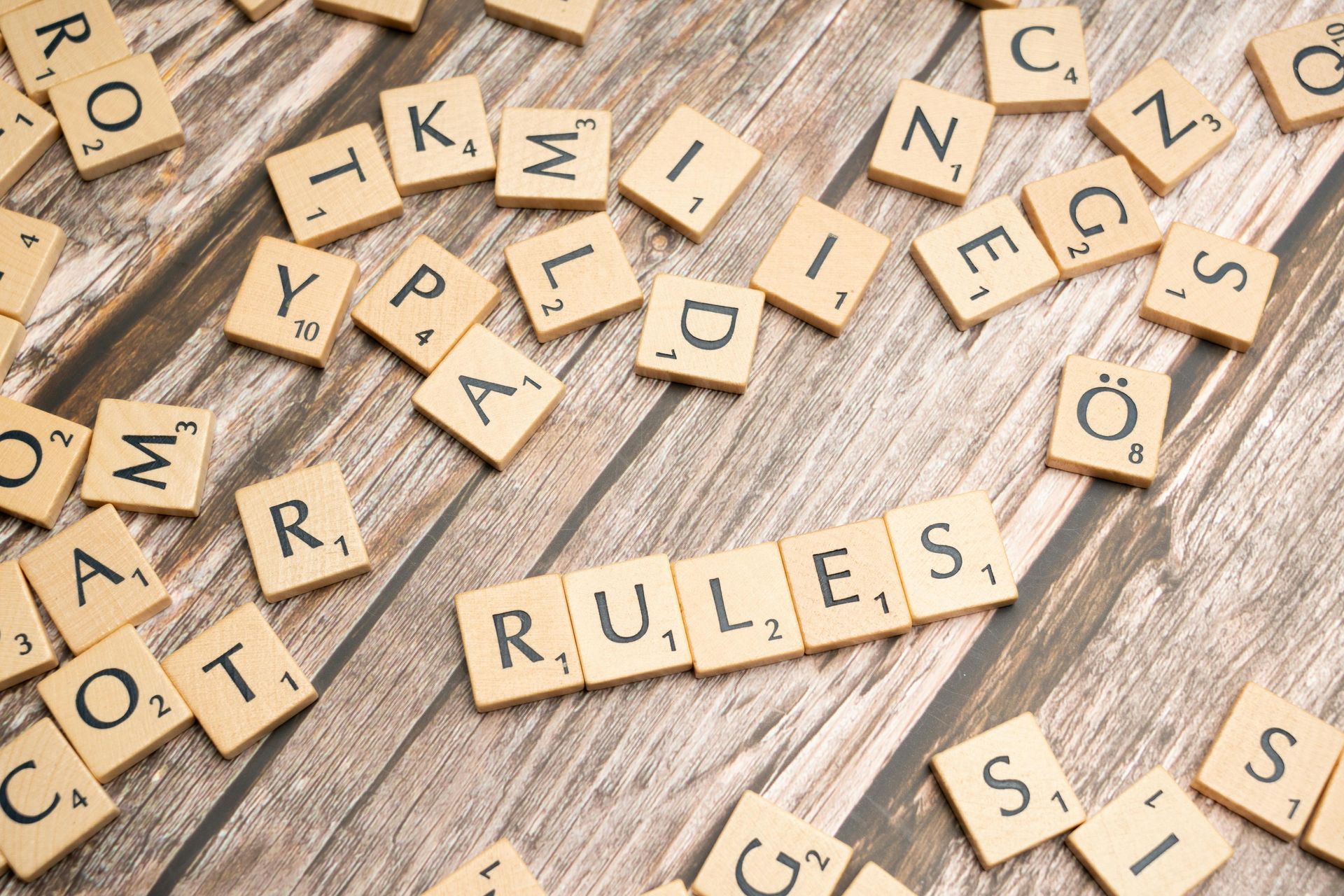 The word rules is written in scrabble tiles on a wooden table.