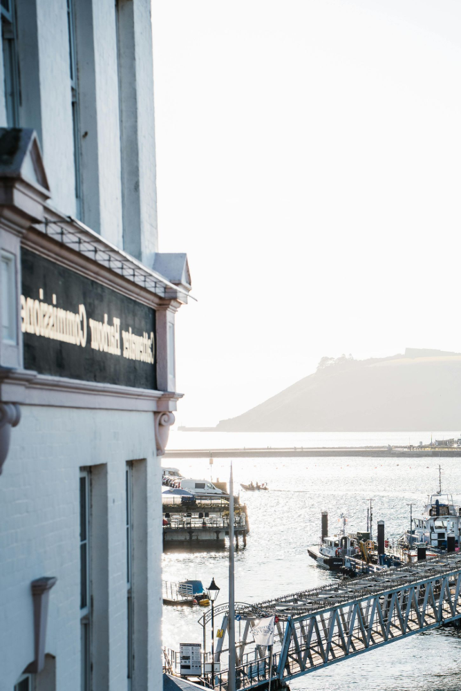 Dock with boats in a harbor, viewed from a white building on a sunny day.