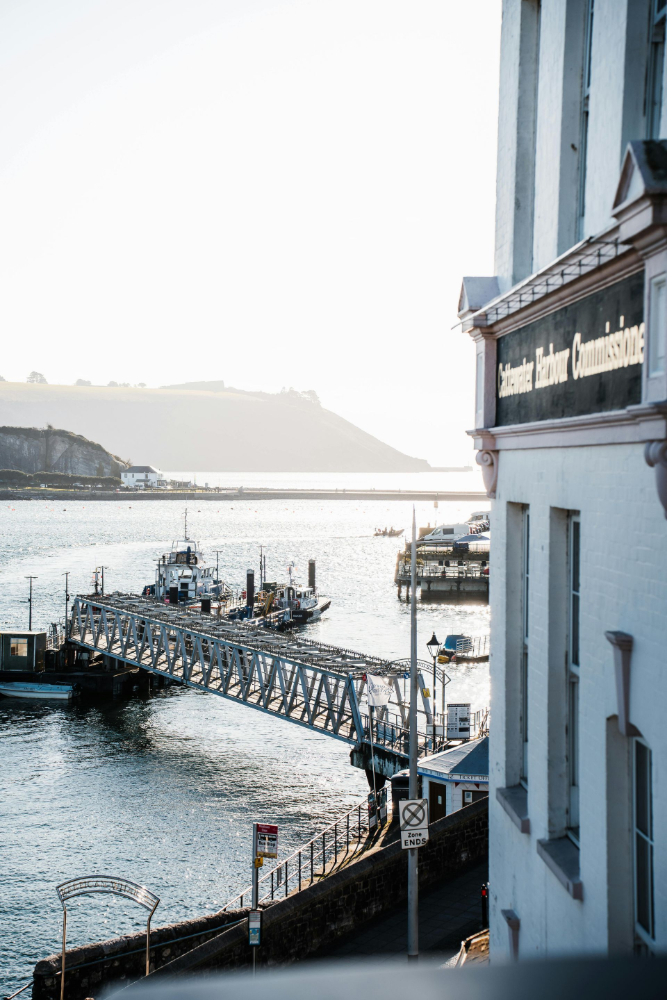 Harbor scene with a pier, buildings, and water, under bright sunlight.