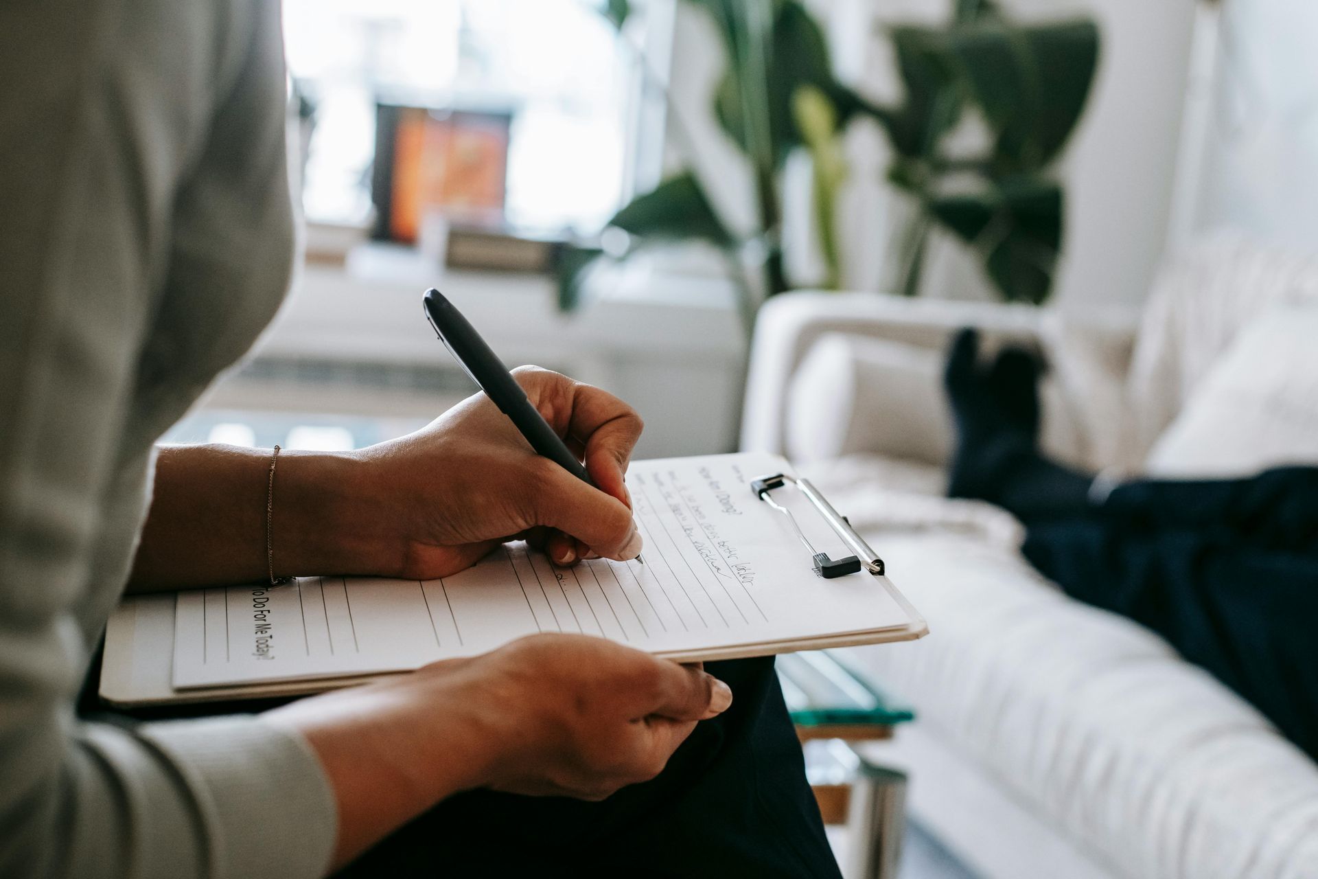 A woman is sitting on a couch writing on a clipboard.