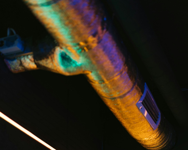 Black corner room with neon light frame, illuminated air duct overhead.