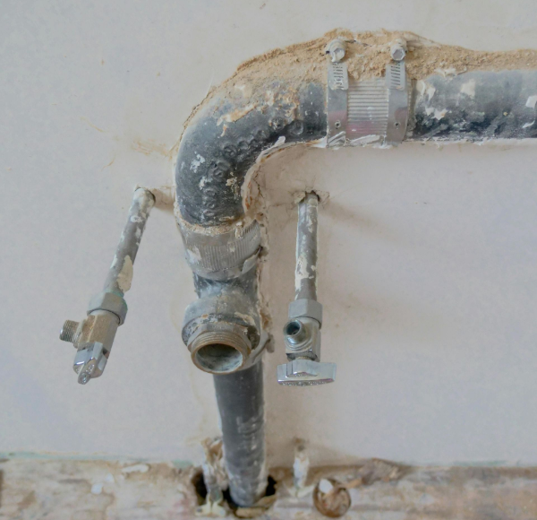 Gray and black pipes emerging from a wall, dusty, with cut-off stubs and connections.