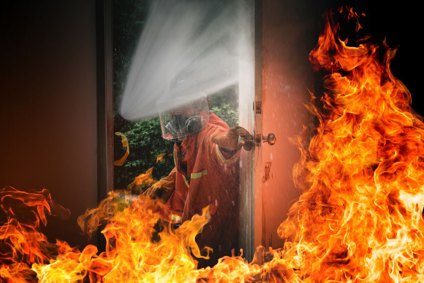 A fireman is spraying water on a fire in a doorway.