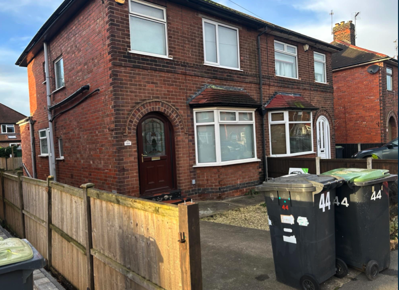 A brick house with a wooden fence and trash cans in front of it.