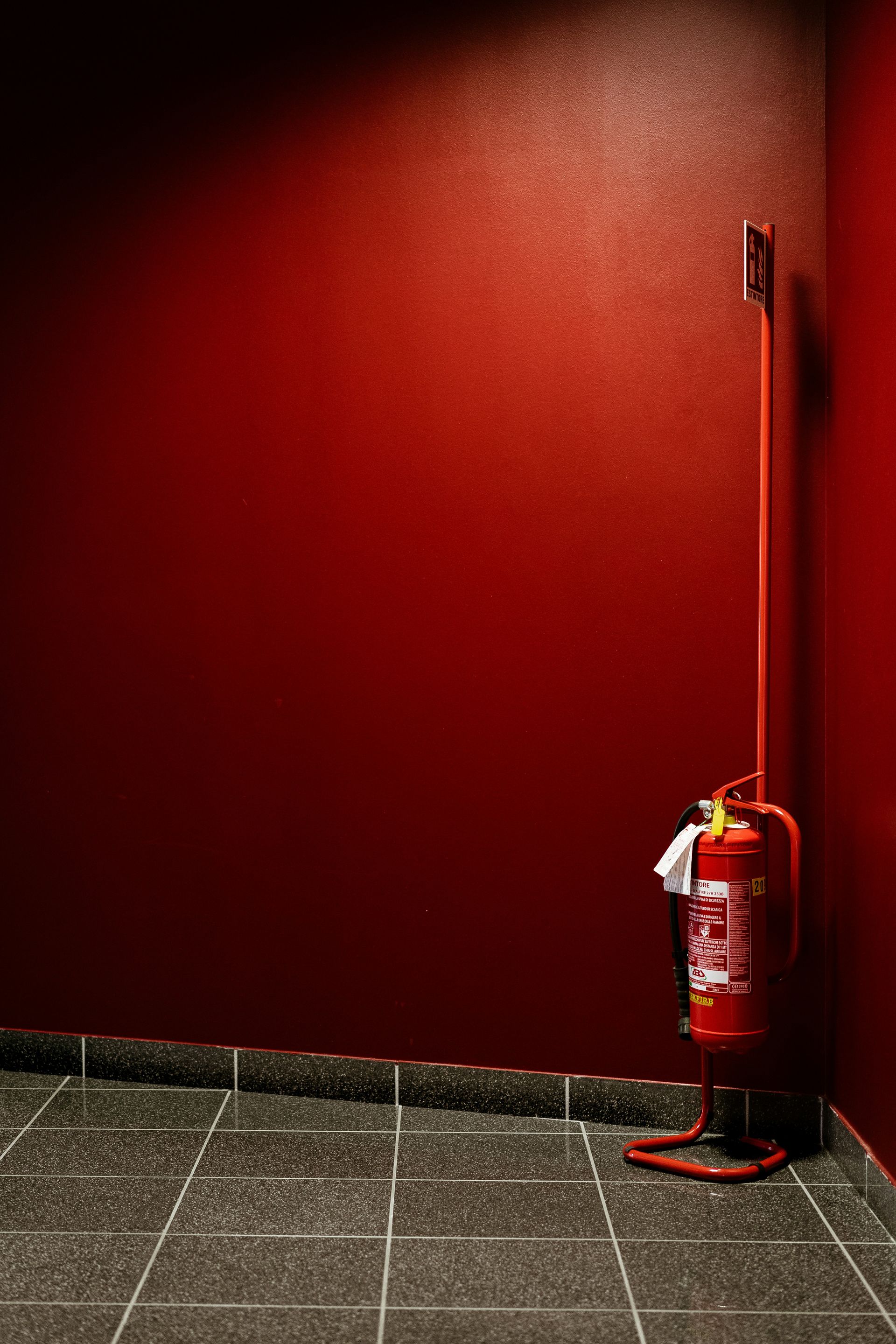 A red fire extinguisher is sitting in a corner of a room next to a red wall.