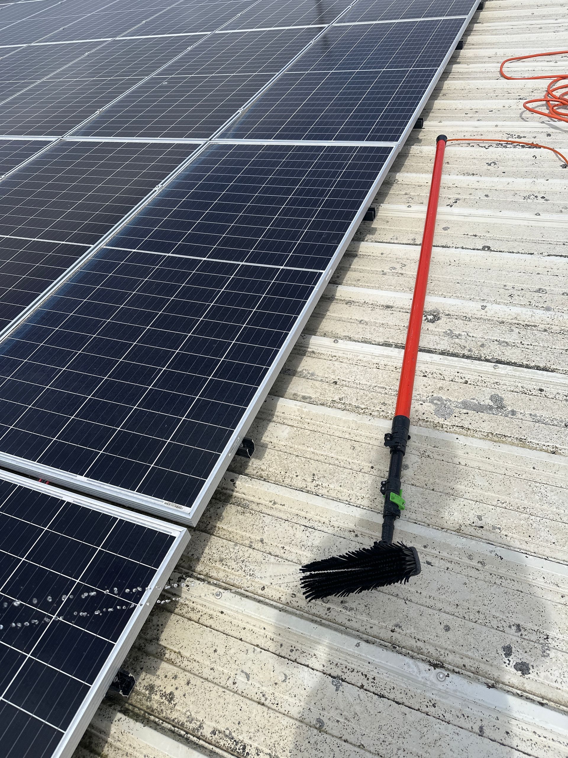 A broom is sitting on top of a roof next to solar panels.