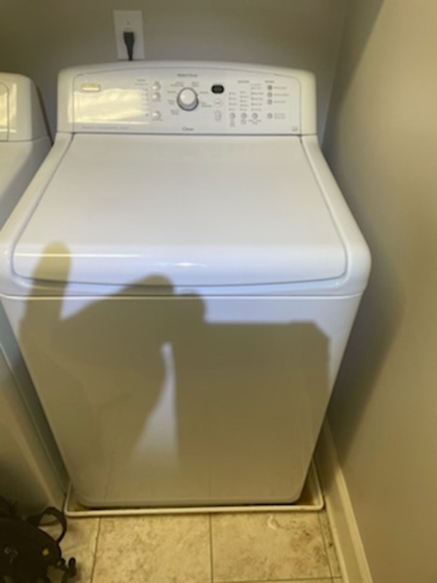A white washing machine is sitting on a tiled floor in a laundry room.