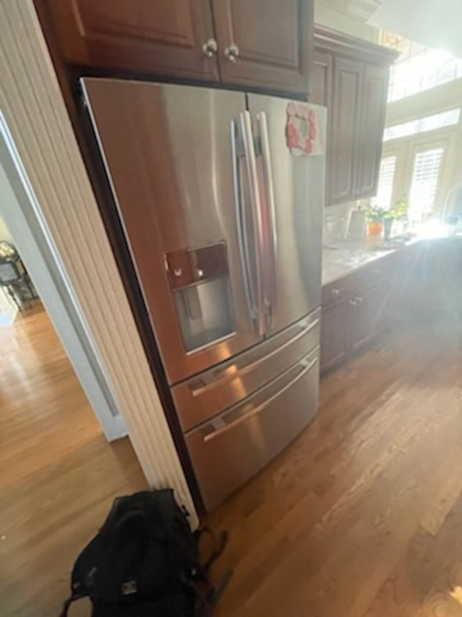 A stainless steel refrigerator is sitting in a kitchen next to a wooden floor.