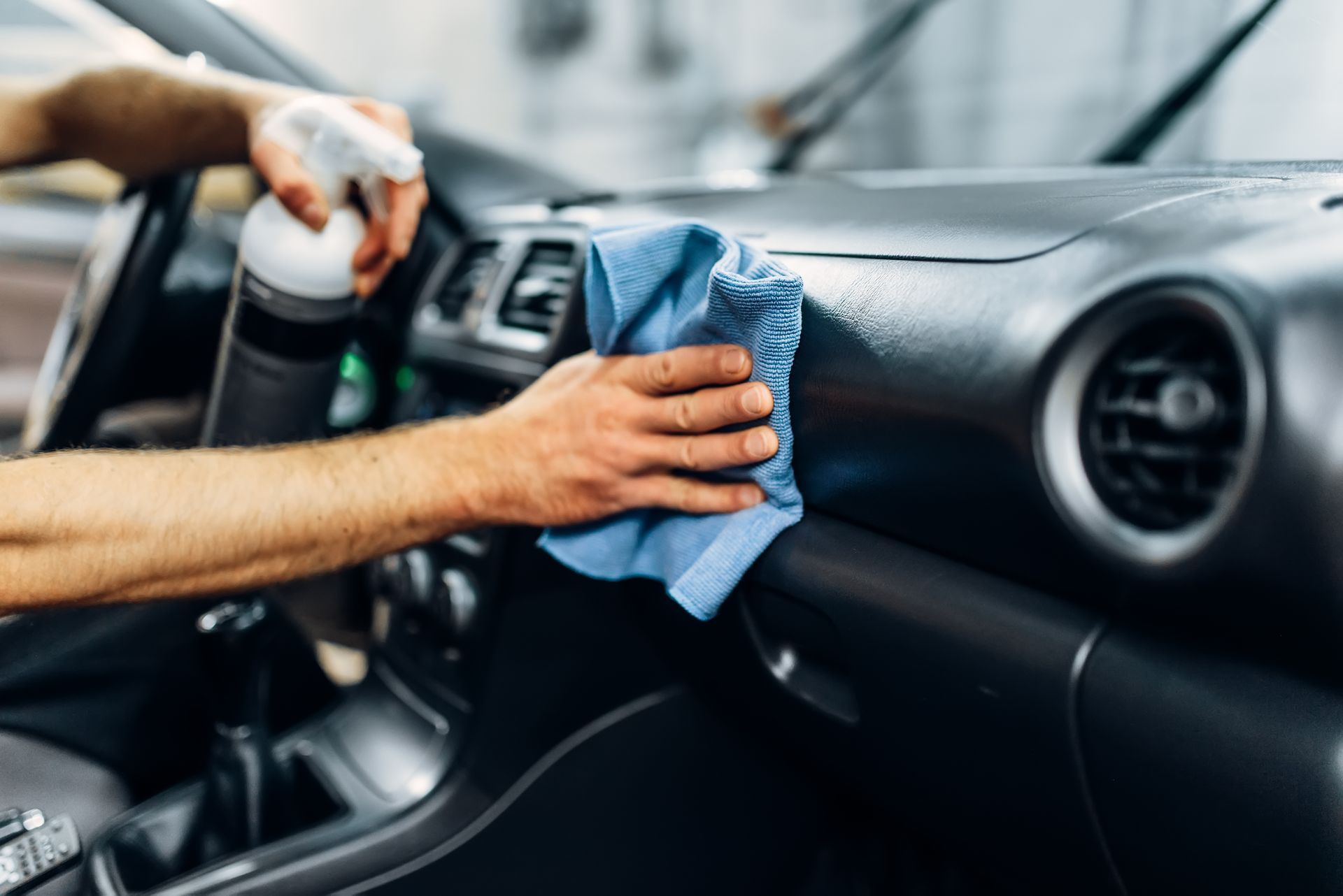 Cleaning car dashboard with a blue cloth and spray bottle