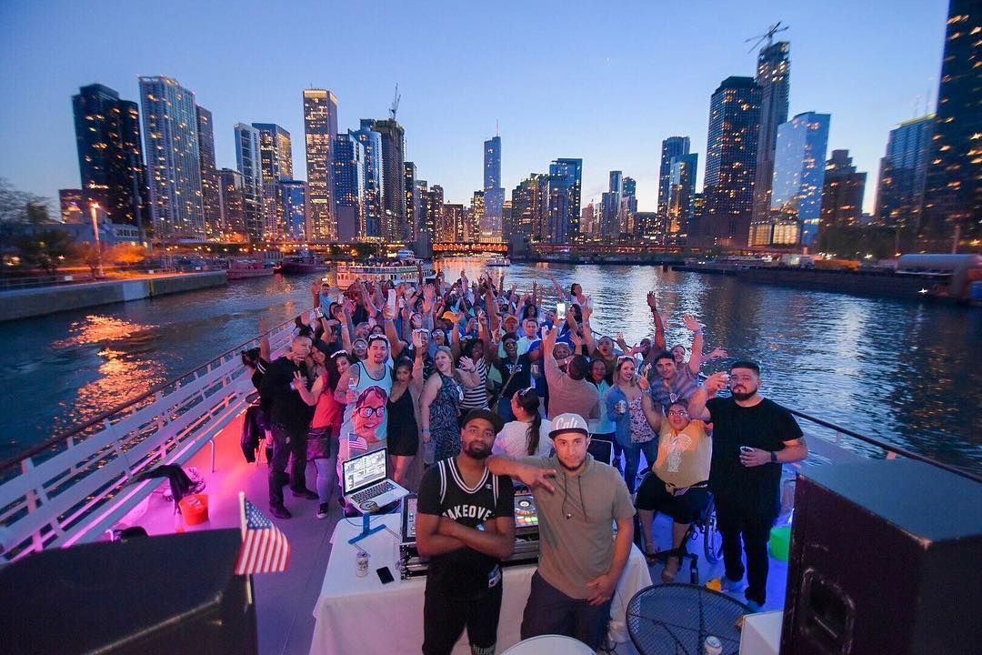 A group of people are standing on a boat in the water with a city skyline in the background.