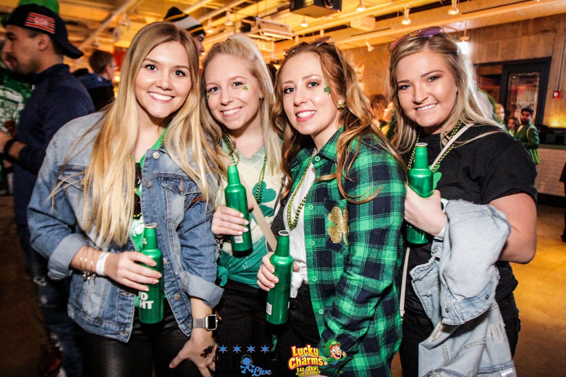 A group of women are posing for a picture while holding green bottles of beer.