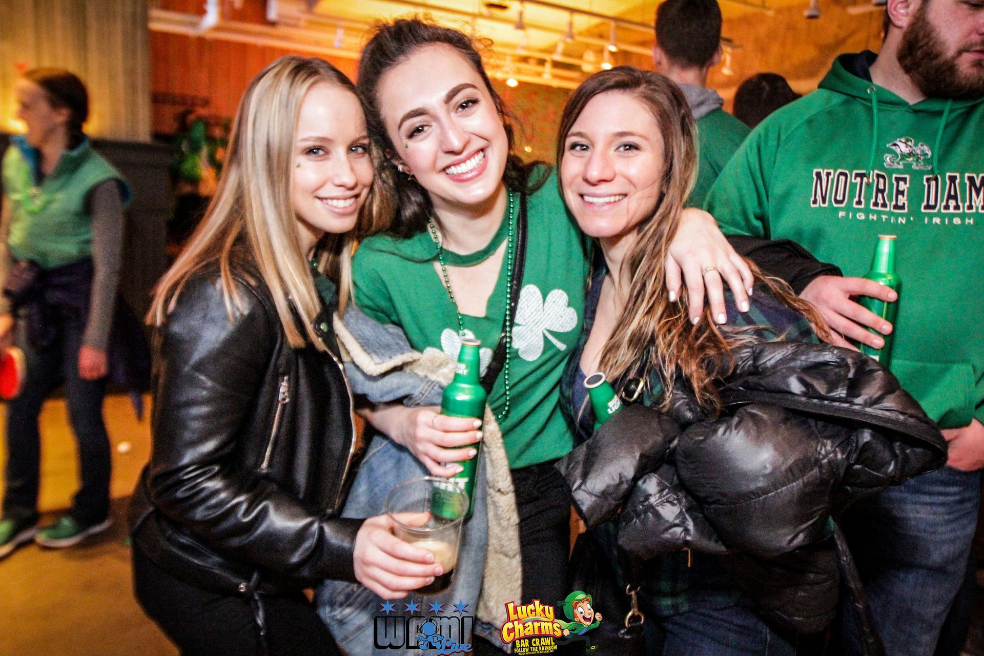 Three women are posing for a picture while one of them is wearing a green shirt with a shamrock on it.
