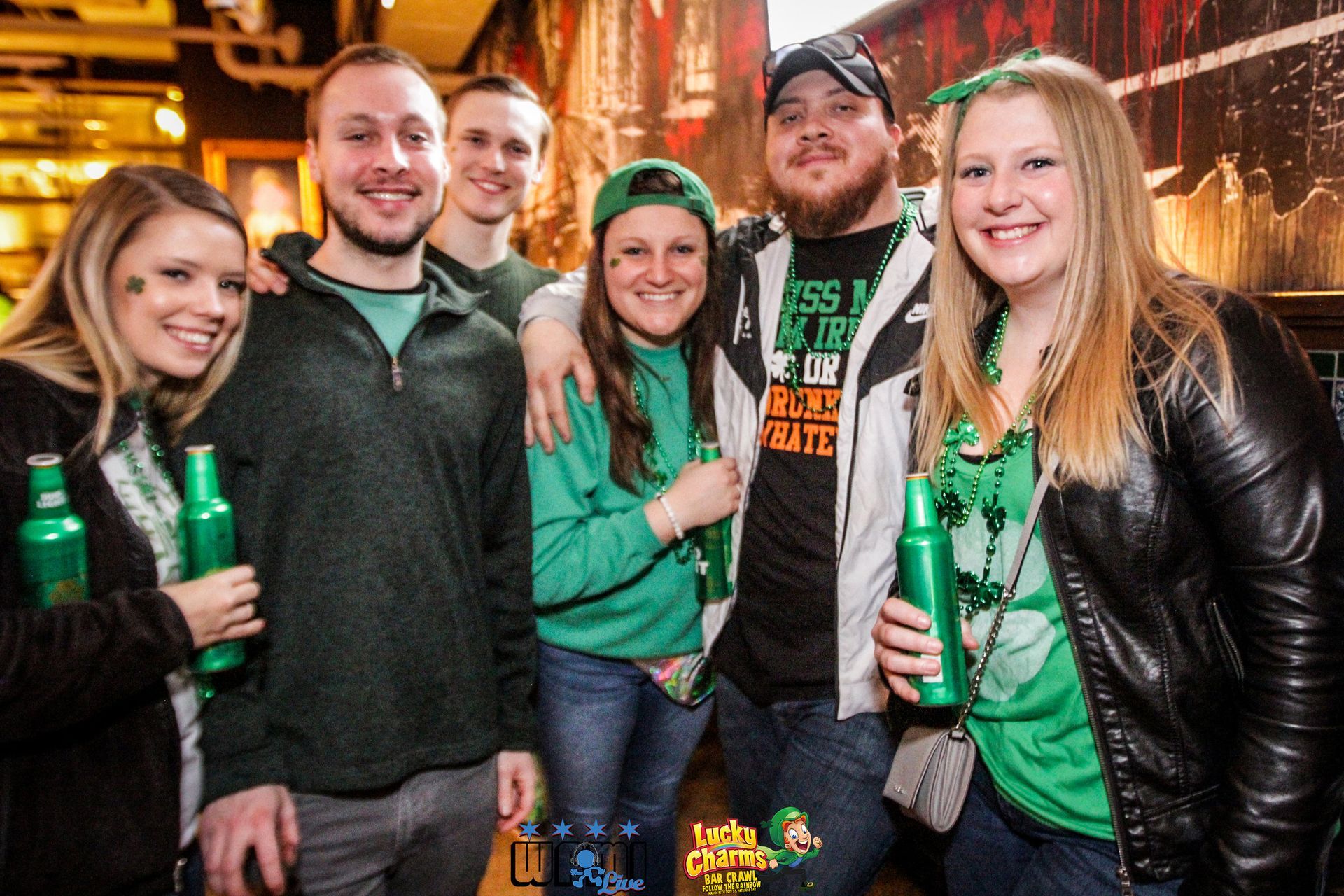 A group of people are posing for a picture while holding green bottles of beer.