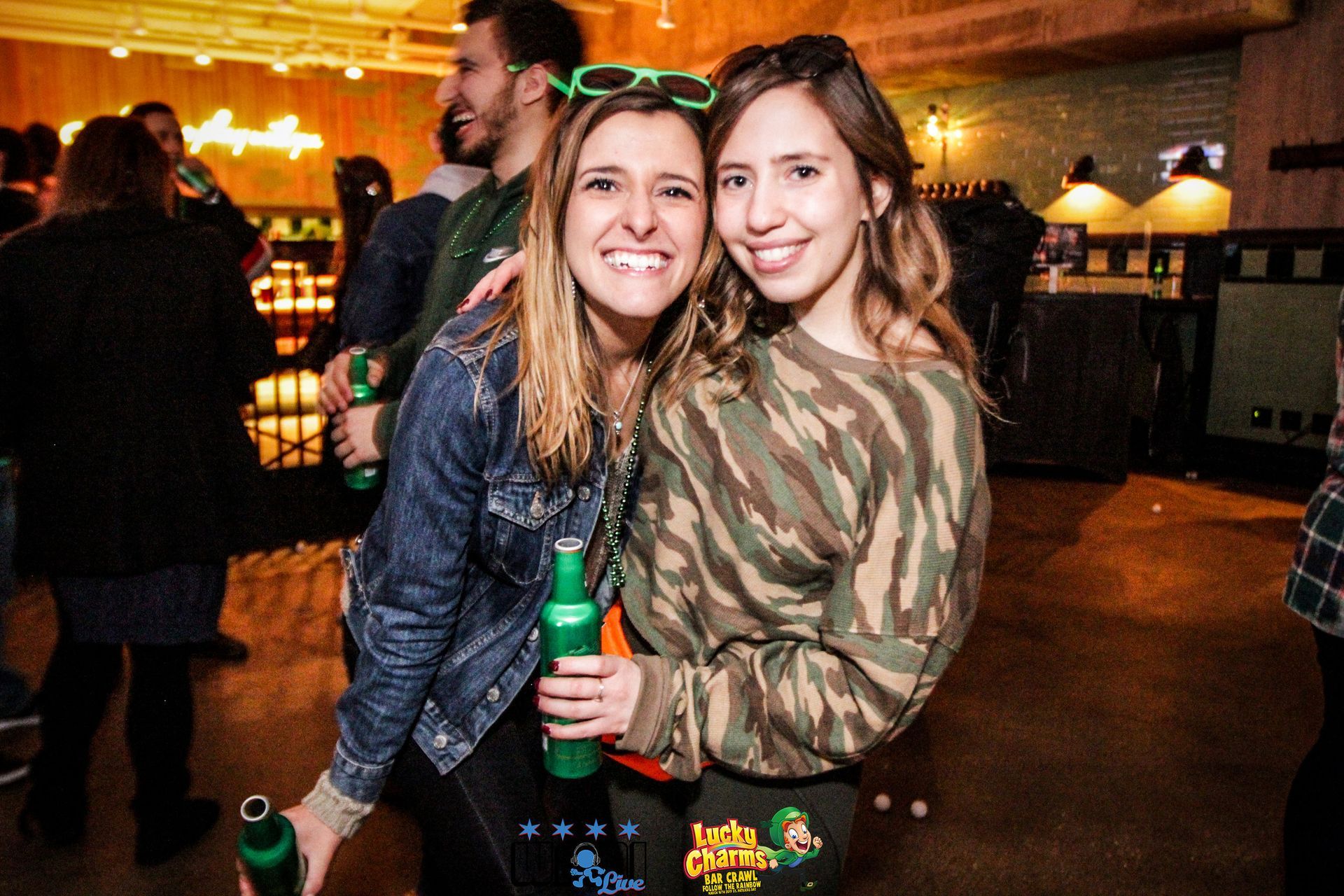 Two women are posing for a picture while holding green bottles of beer.
