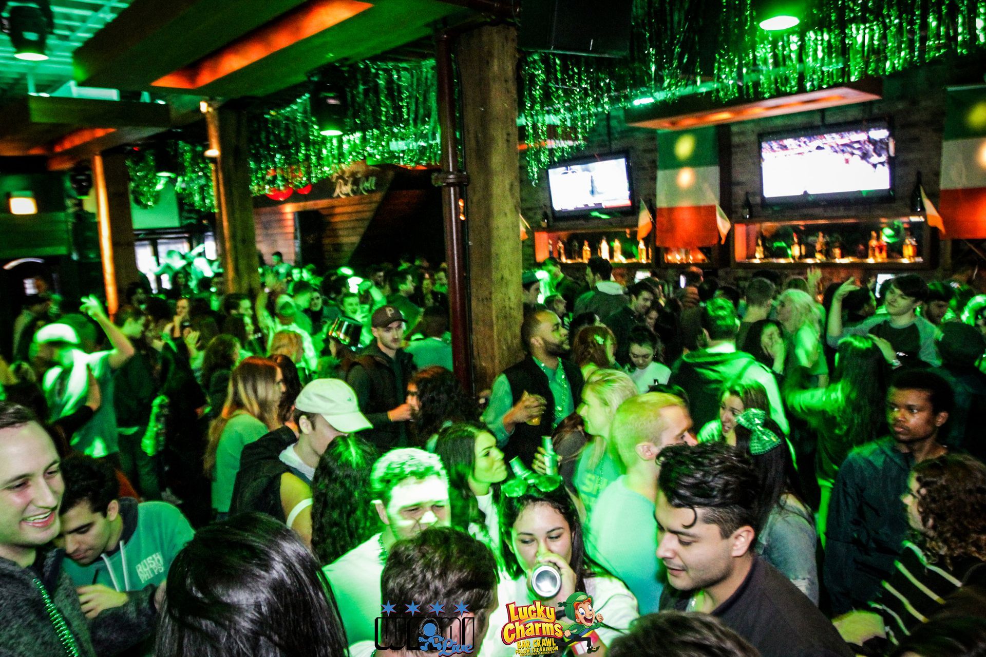 A crowd of people are gathered in a bar with green lights.