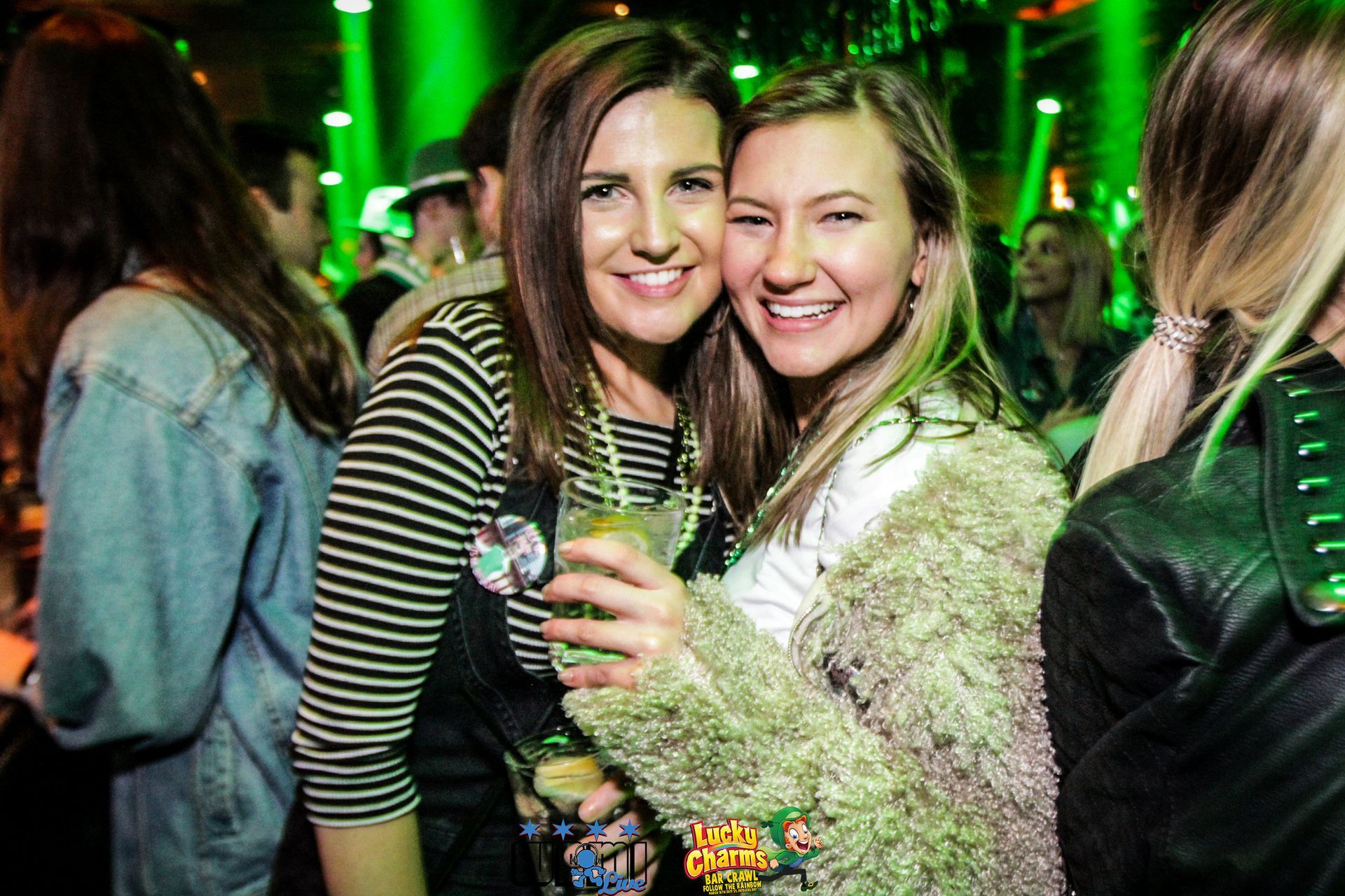 Two women are posing for a picture at a party while holding drinks.