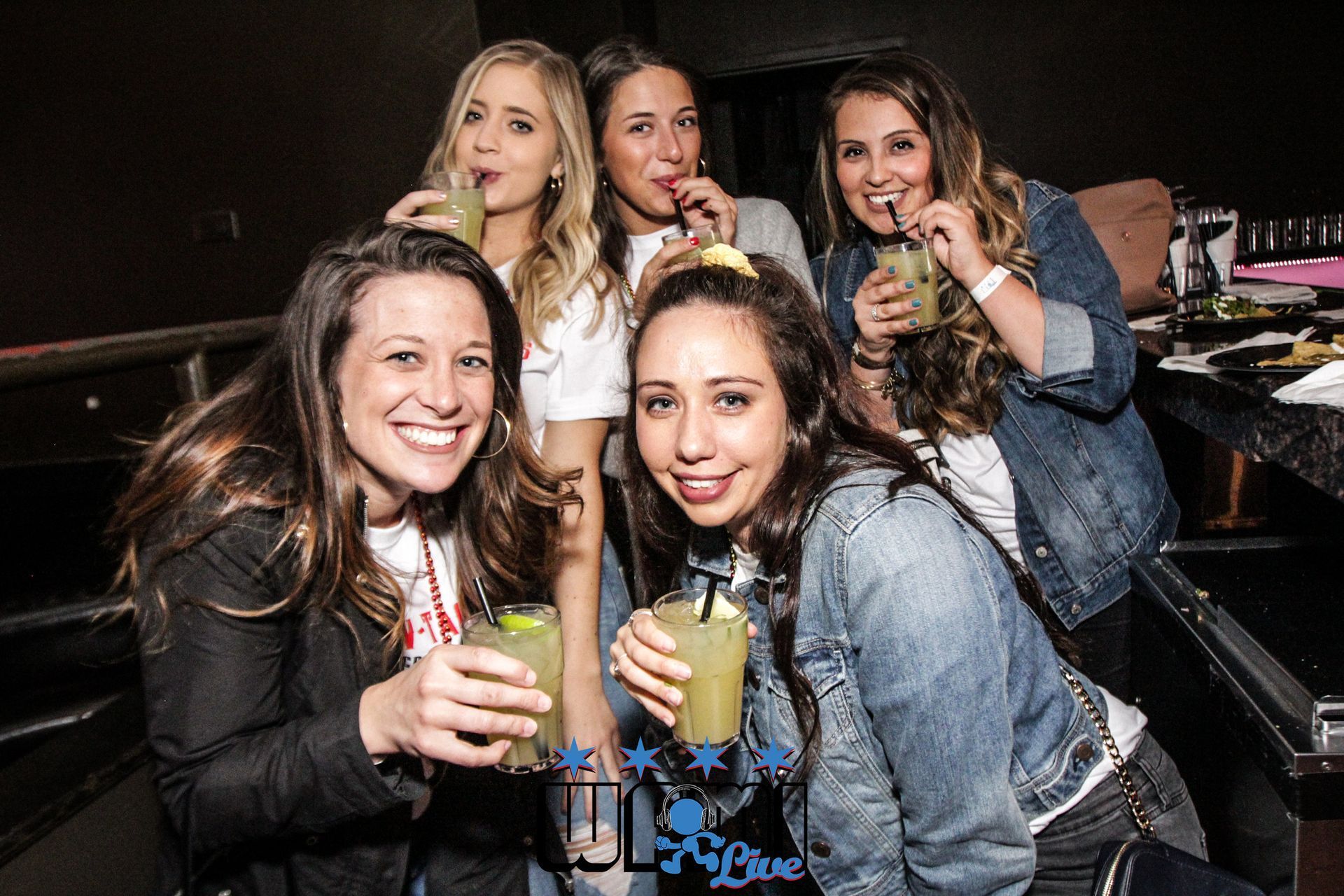 A group of women are sitting at a bar holding drinks.