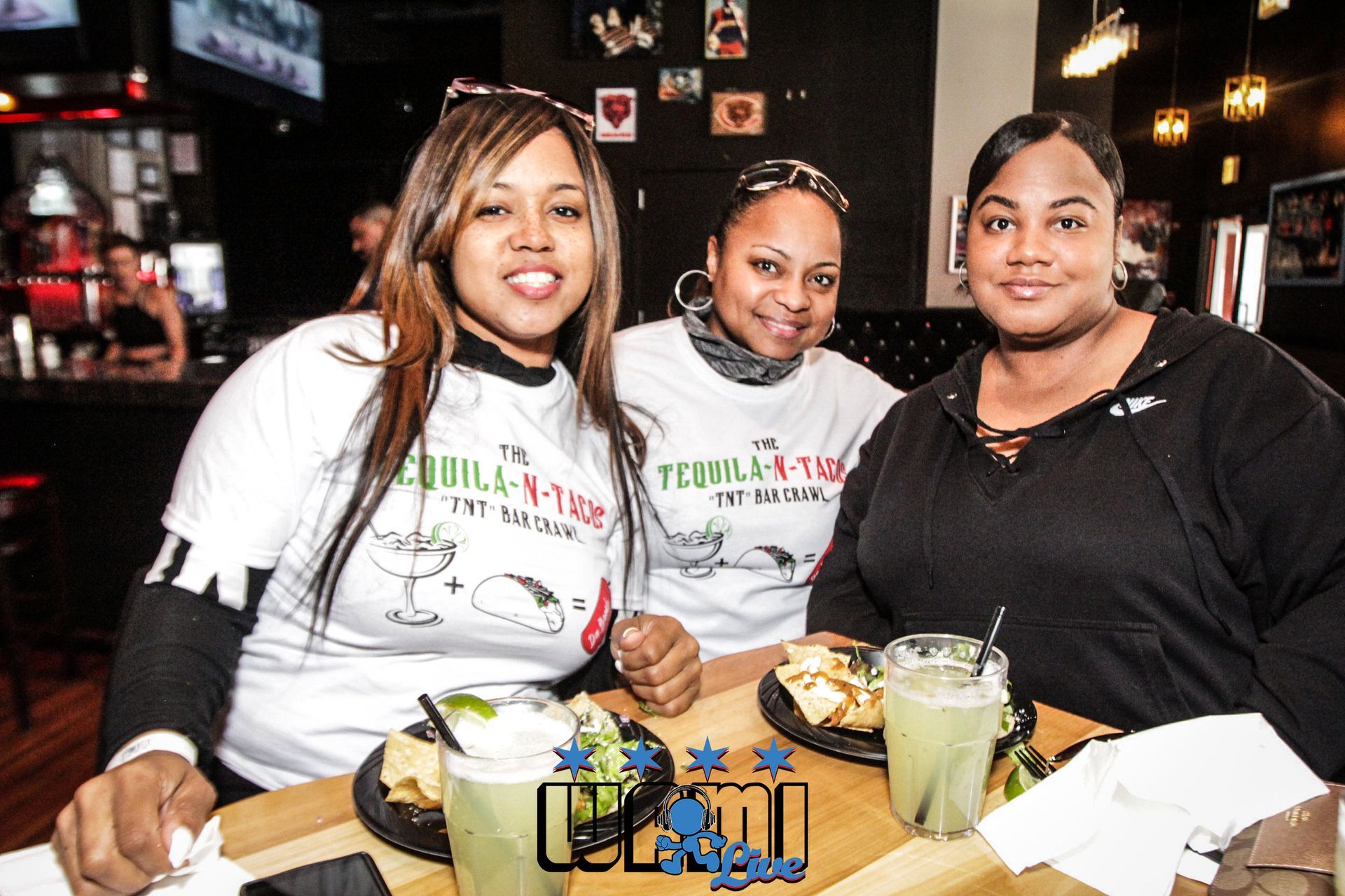 Three women are sitting at a table with plates of food and drinks.