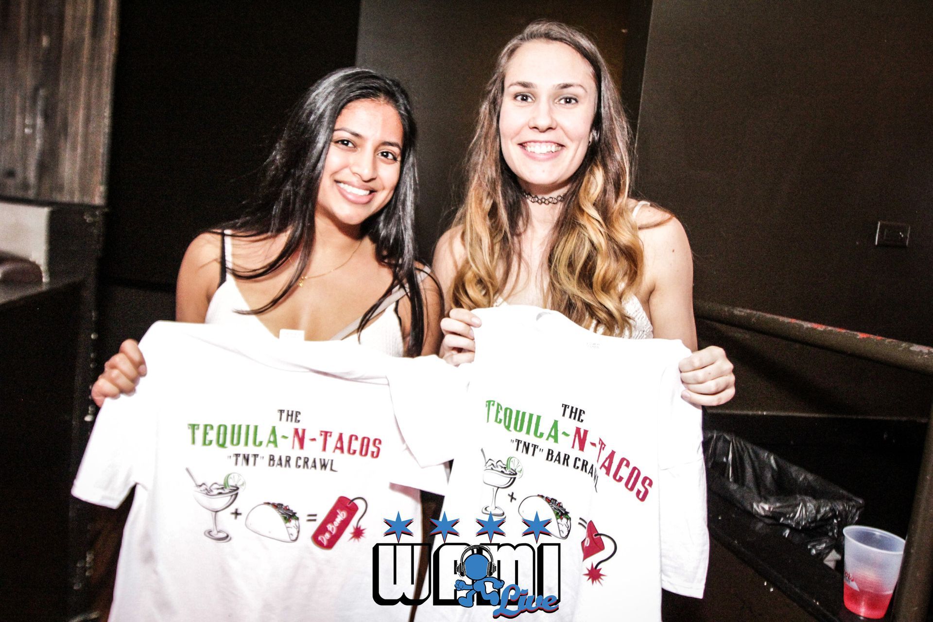 Two women are holding up tequila n tacos t-shirts