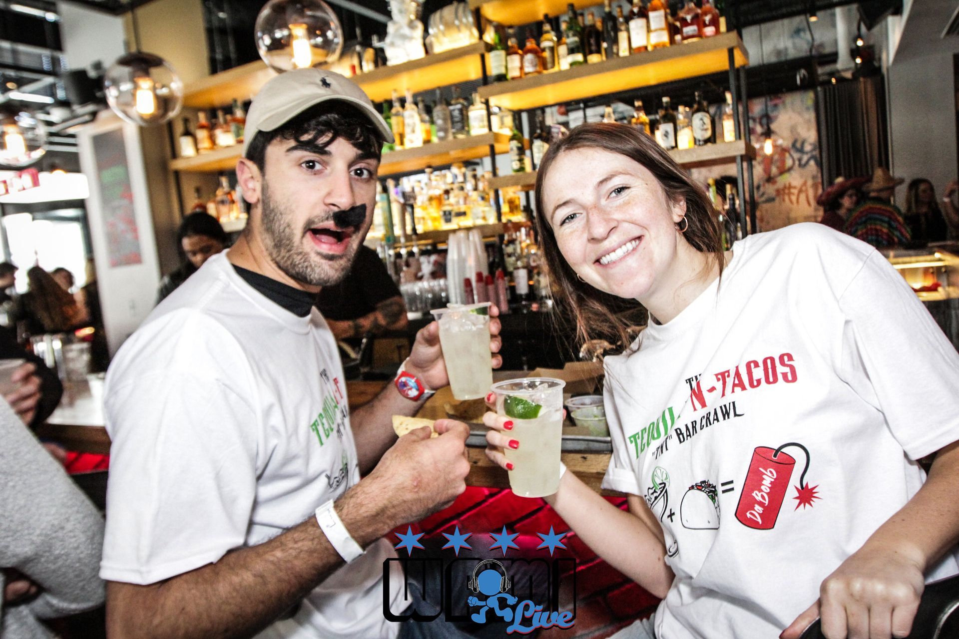 A man and a woman are sitting at a bar holding drinks.