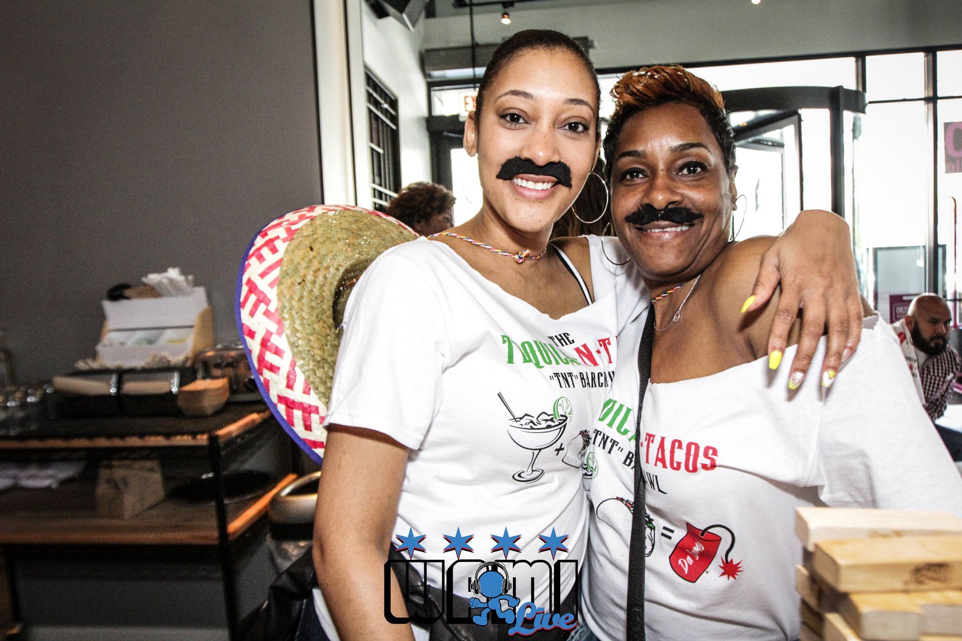 Two women wearing fake mustaches are posing for a picture in a restaurant.