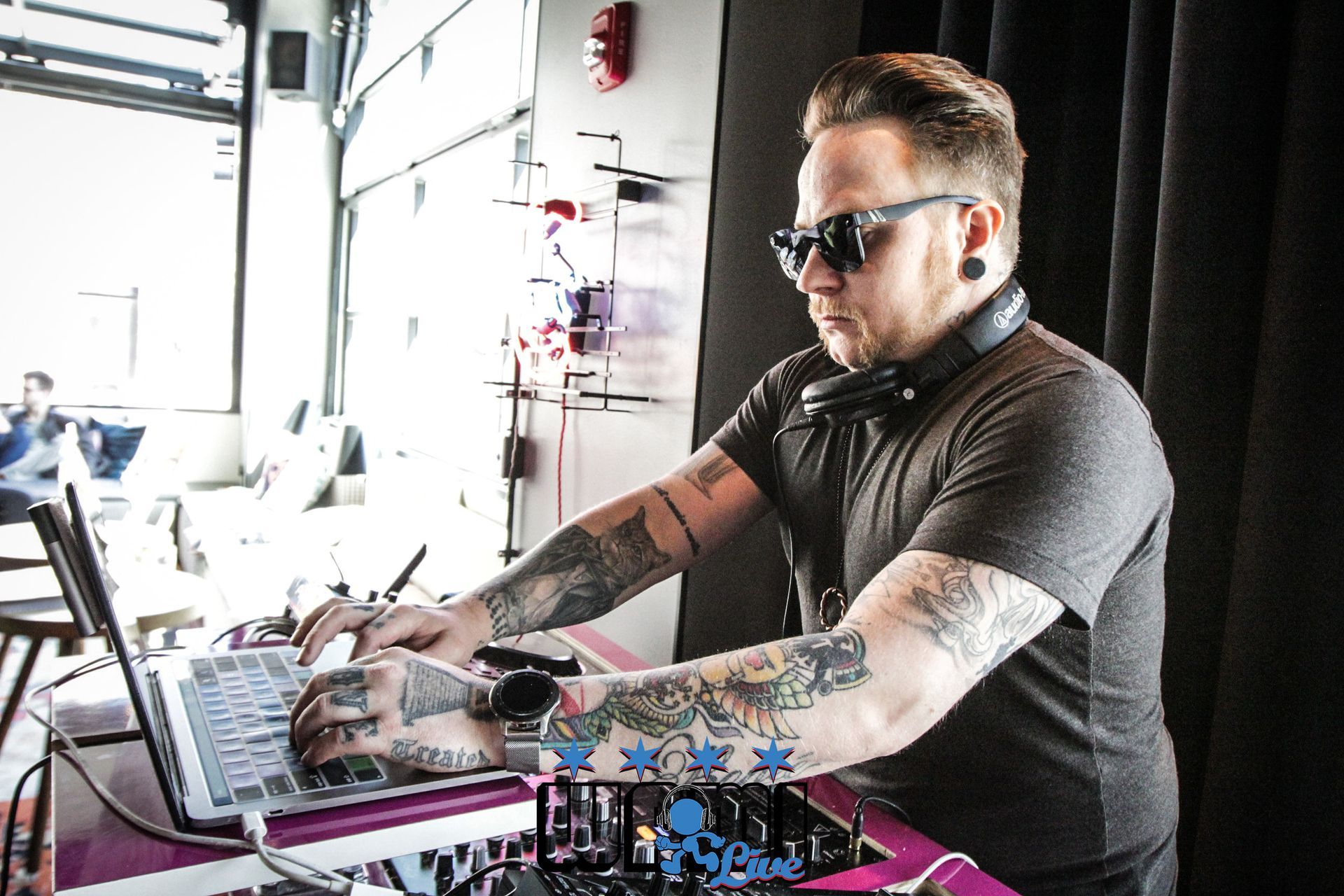 A man with tattoos is using a laptop computer while wearing headphones.