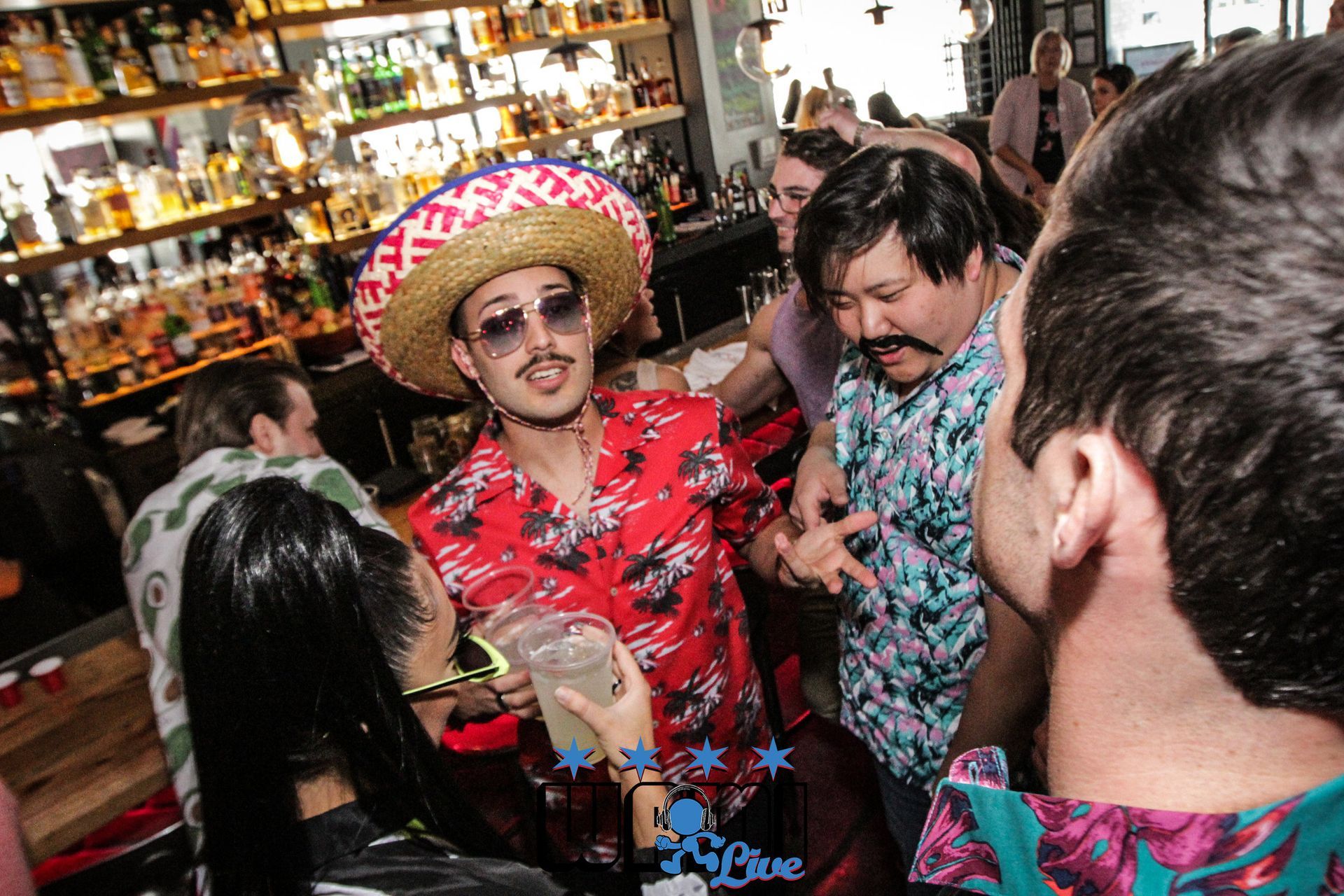 A man wearing a sombrero and sunglasses is dancing with a group of people in a bar.
