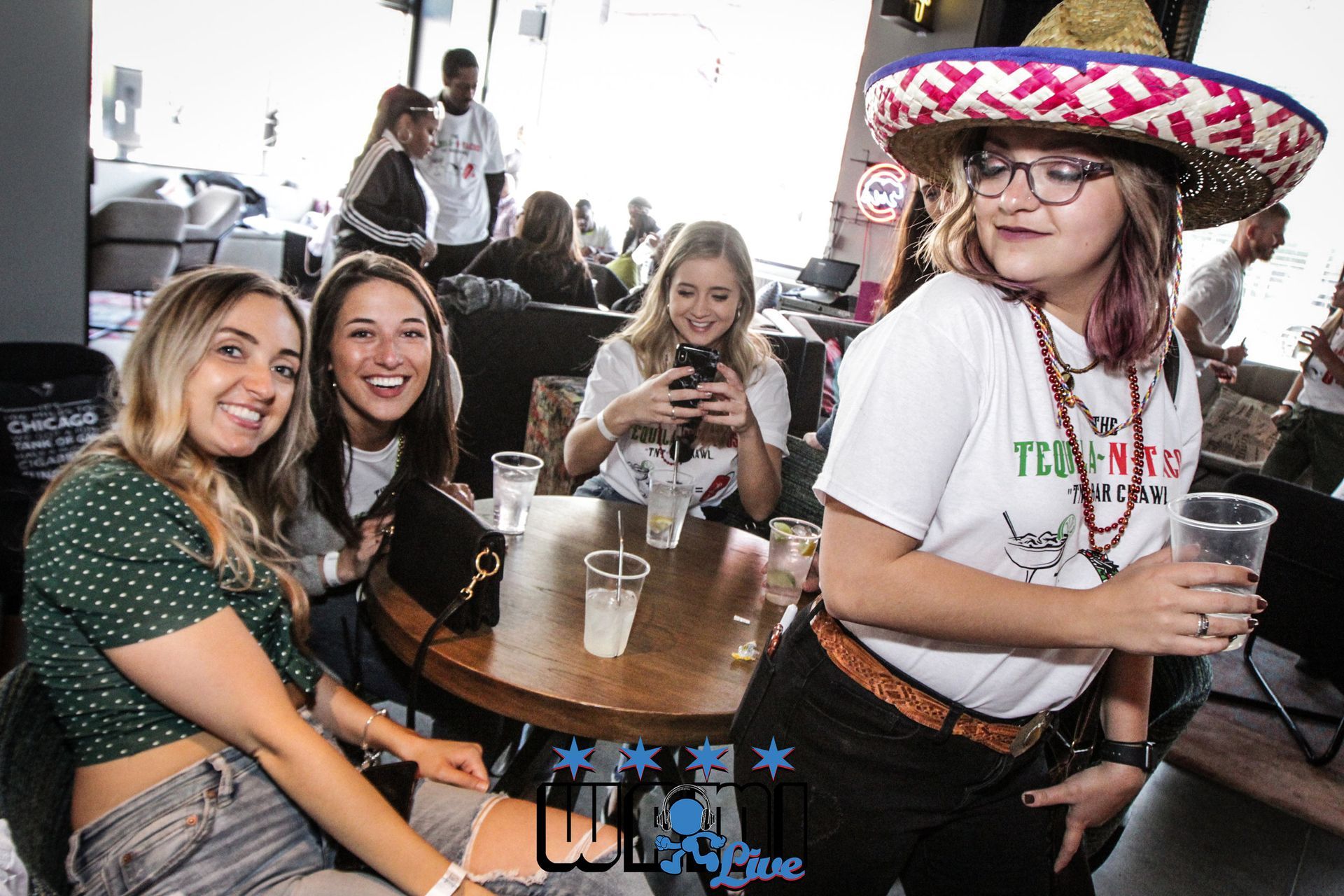 A group of women are sitting at a table in a restaurant . one of the women is wearing a sombrero.