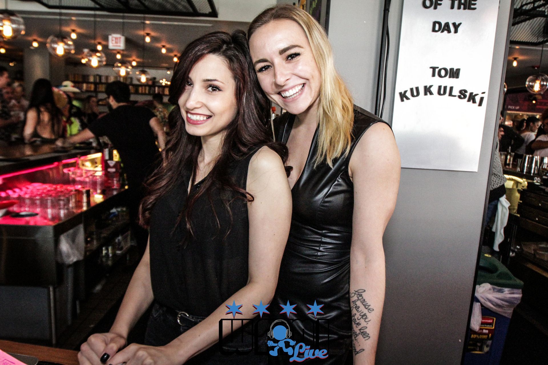 Two women standing next to each other in front of a sign that says tom kukulski