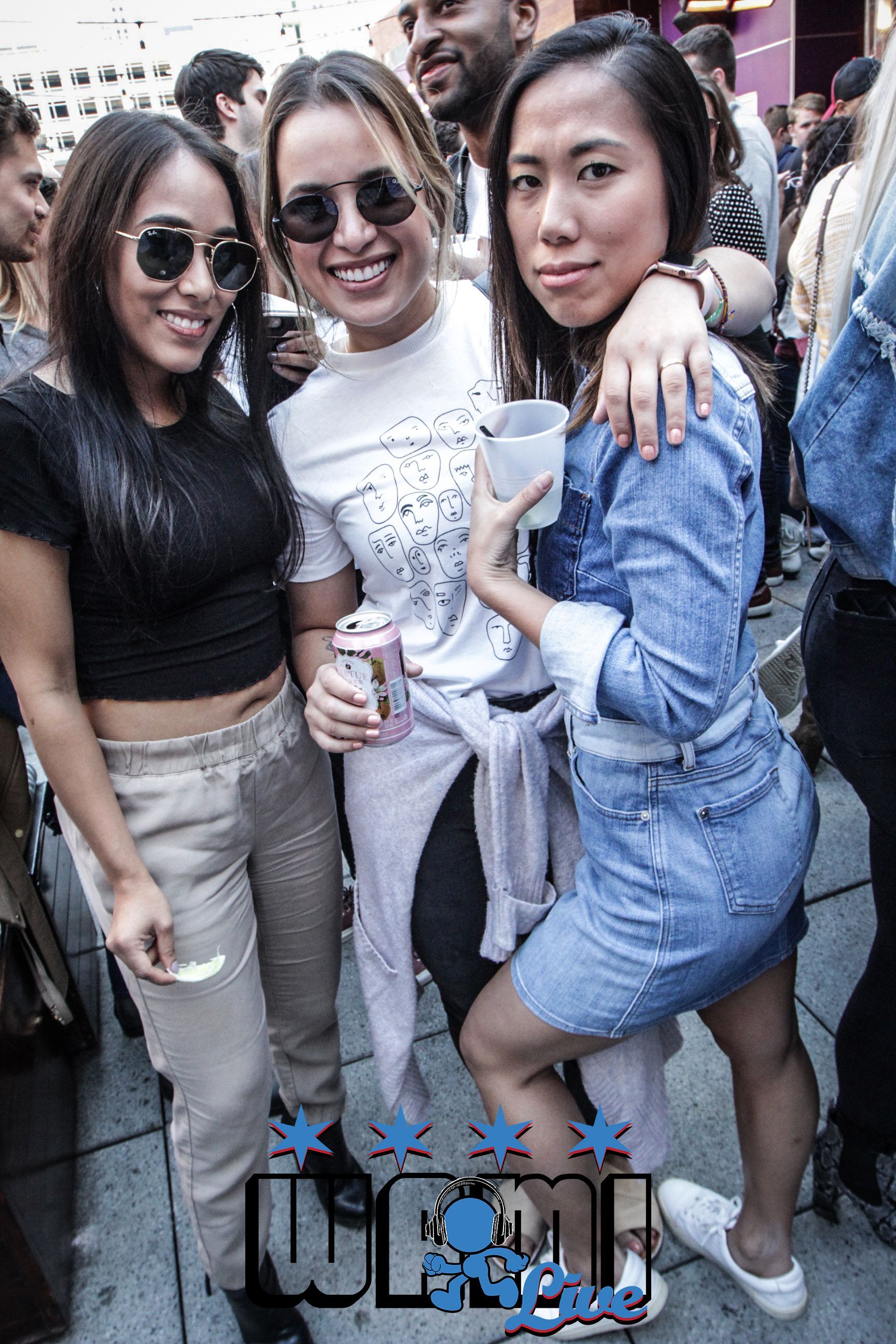 Three women are posing for a picture in a crowd of people.