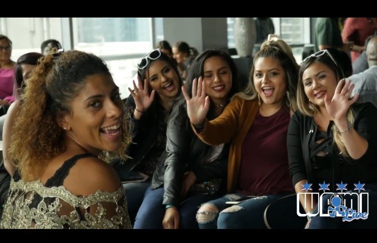A group of women are sitting next to each other and waving at the camera.