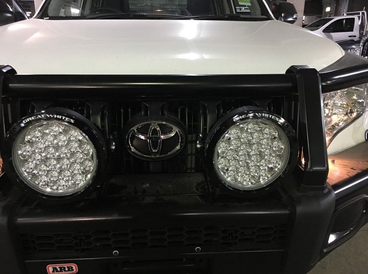 The front of a white toyota truck with a black bumper and lights.