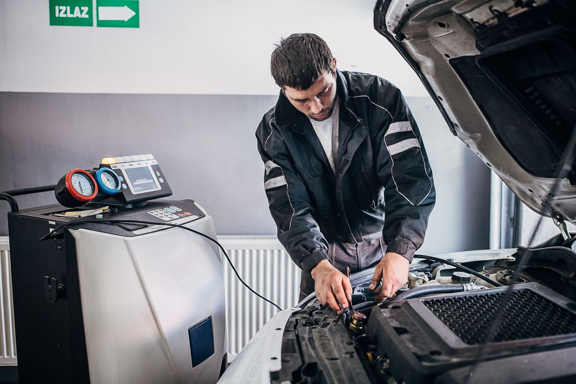 A man is working on a car with the hood open in a garage.