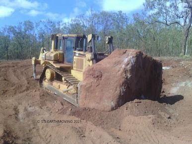 A Bulldozer is Moving a Large Rock in the Dirt — STJ Earthmoving in Mareeba, QLD