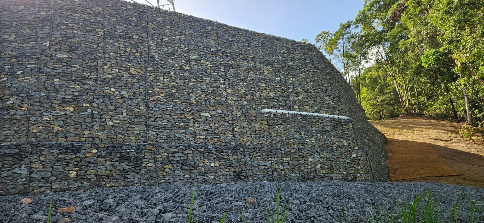 A Gabion Wall Filled With Rocks Slopes Upward, Next to Trees — STJ Earthmoving in Mareeba, QLD