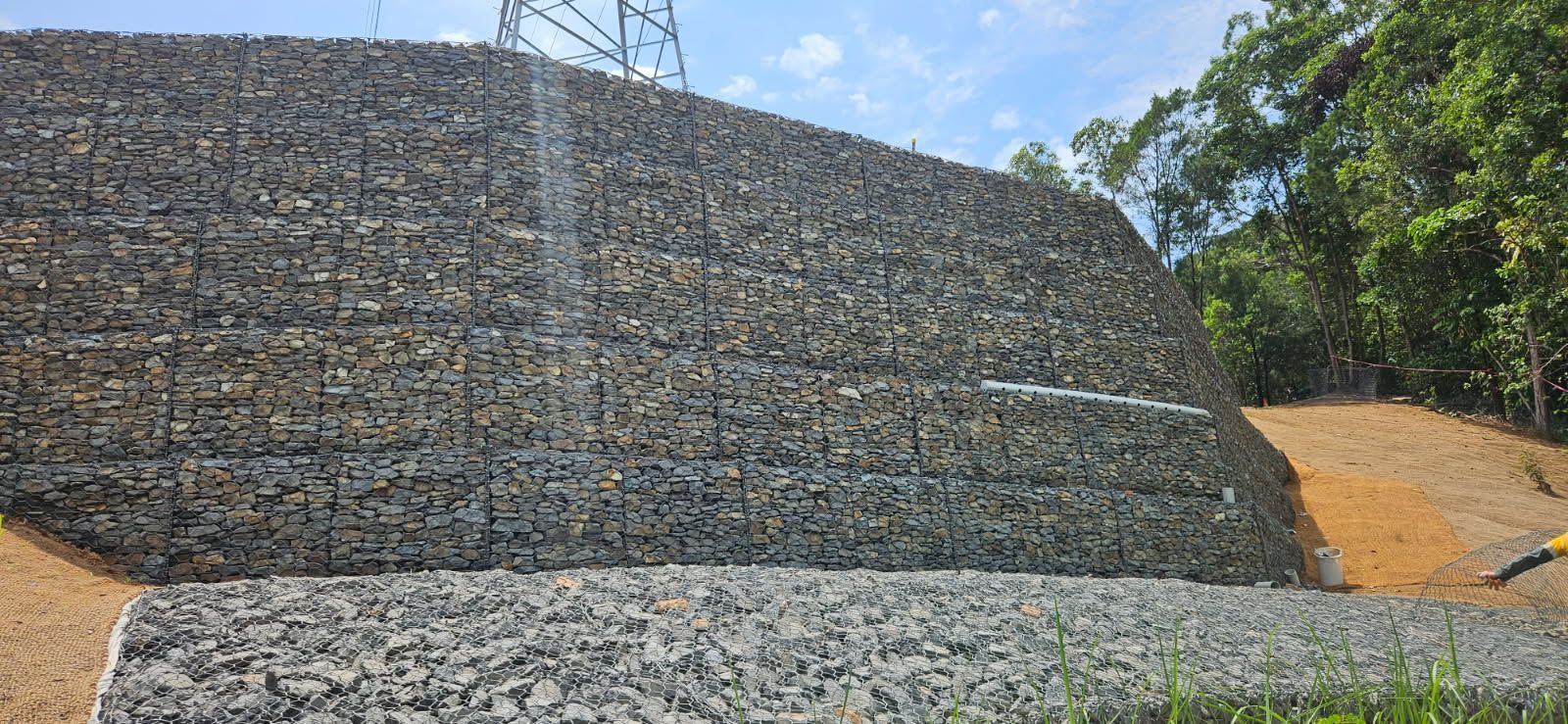 Gabion Retaining Wall With Power Lines, Rocks, and Vegetation — STJ Earthmoving in Mareeba, QLD