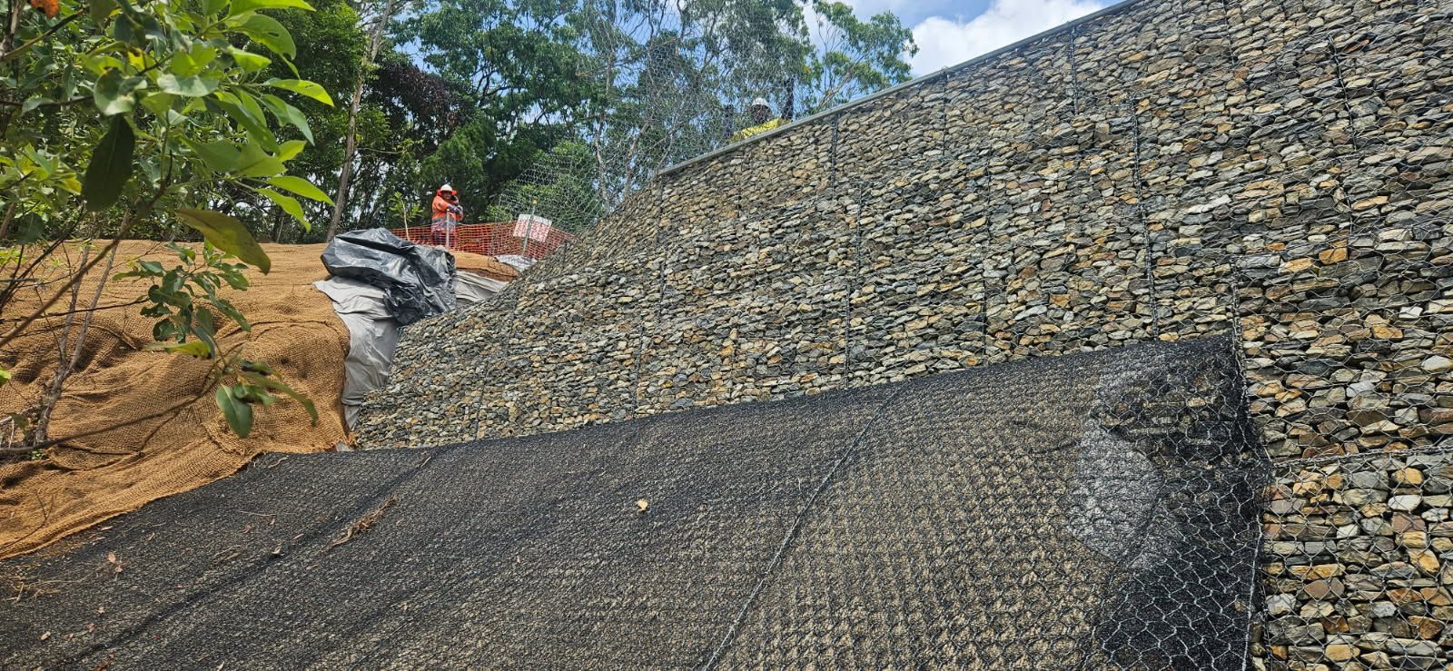 A Retaining Wall Made of Rocks With a Black Mesh — STJ Earthmoving in Mareeba, QLD