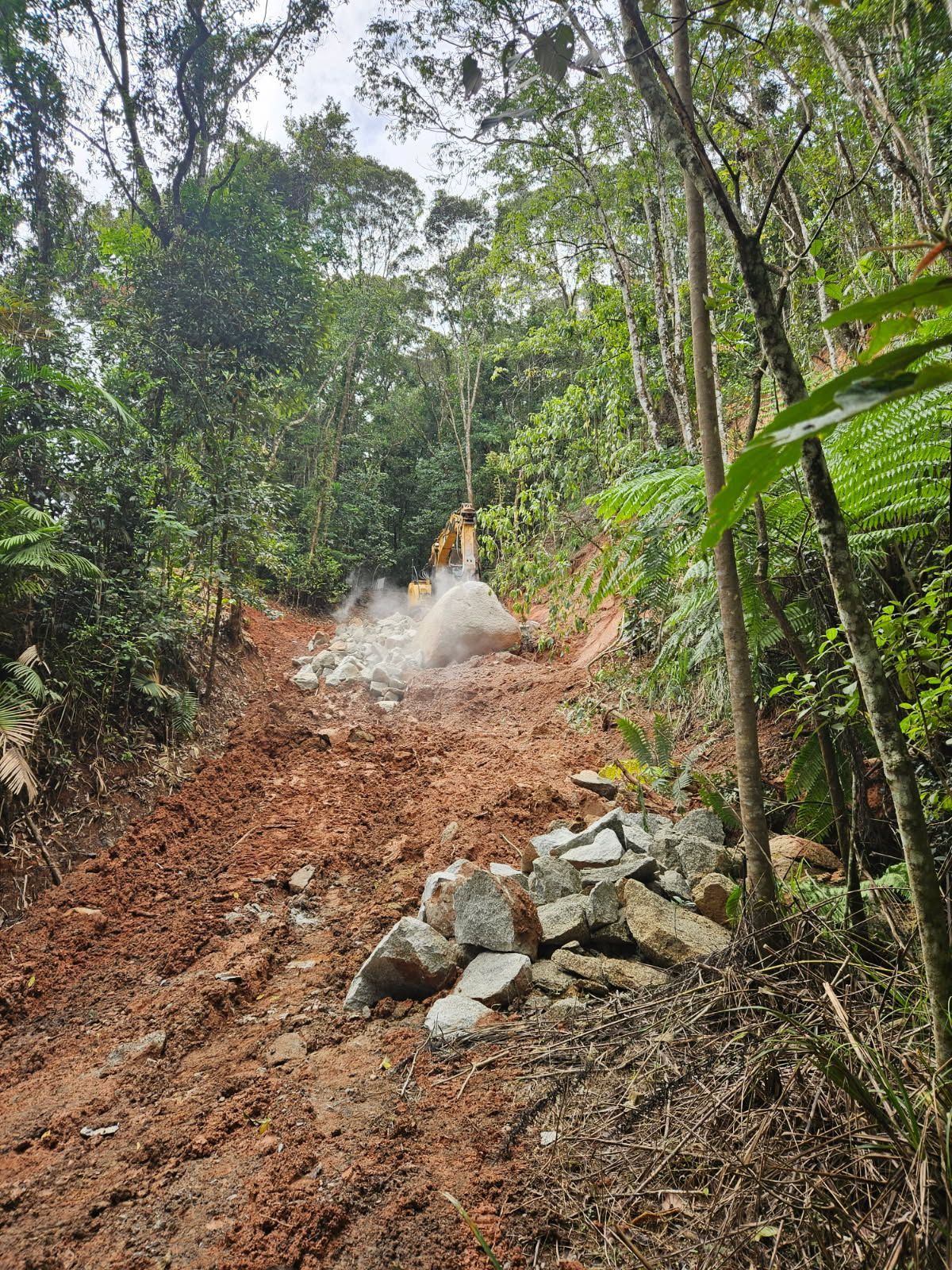 Excavator Clearing Rocks and Dirt on a Hillside Road in a Forest — STJ Earthmoving in Mareeba, QLD