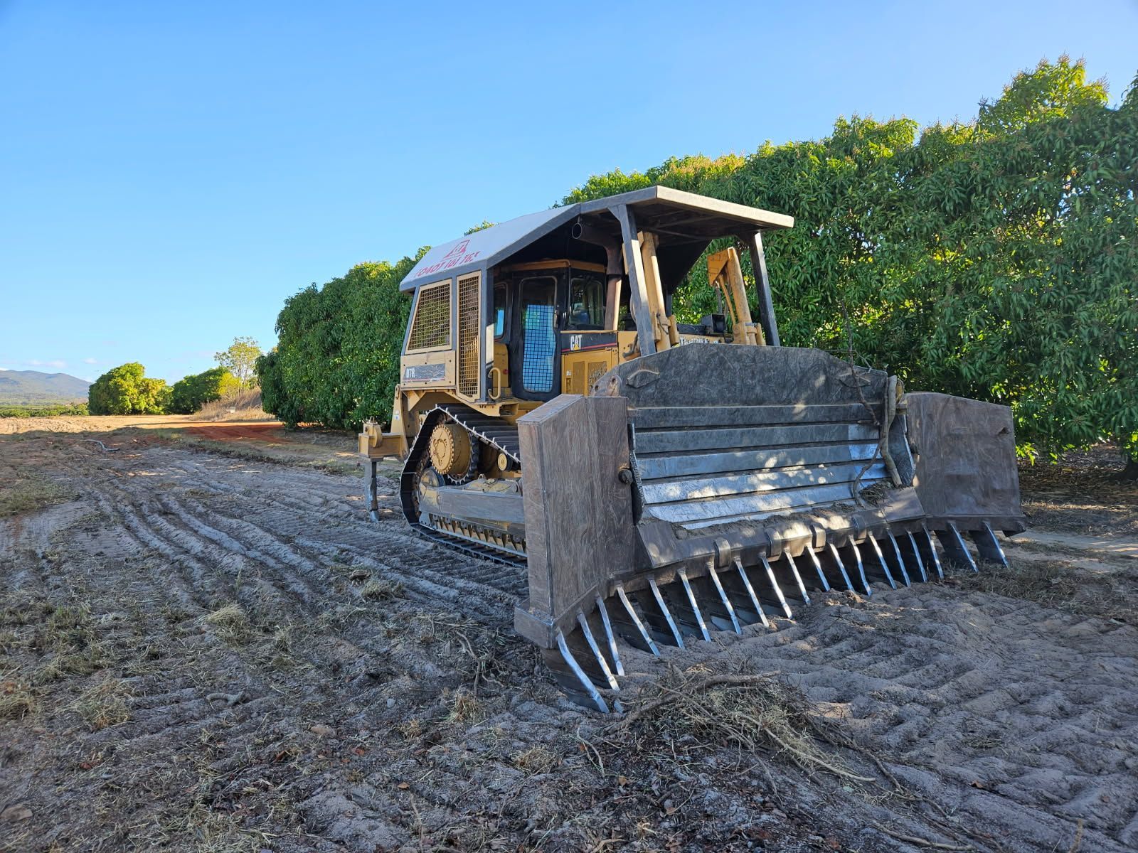 Bulldozer With Rake Attachment on Dirt Field, Trees in Background — STJ Earthmoving in Mareeba, QLD