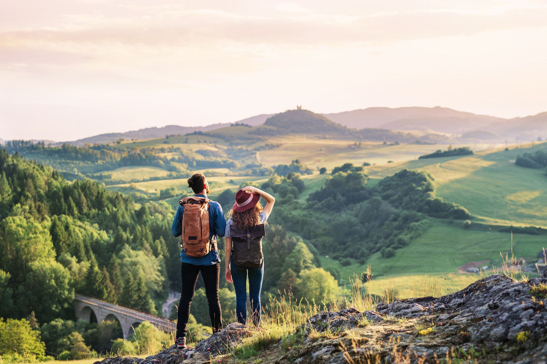 A man and a woman are standing on top of a hill looking at the landscape.
