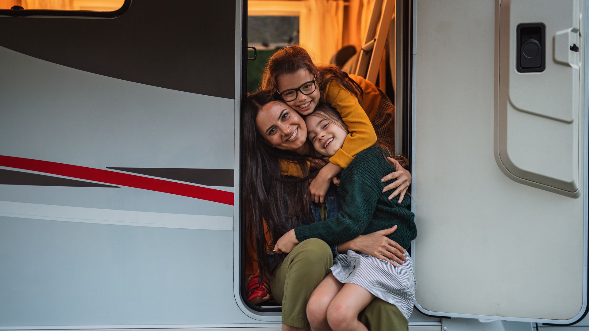 A woman and two children are sitting in the doorway of a camper.