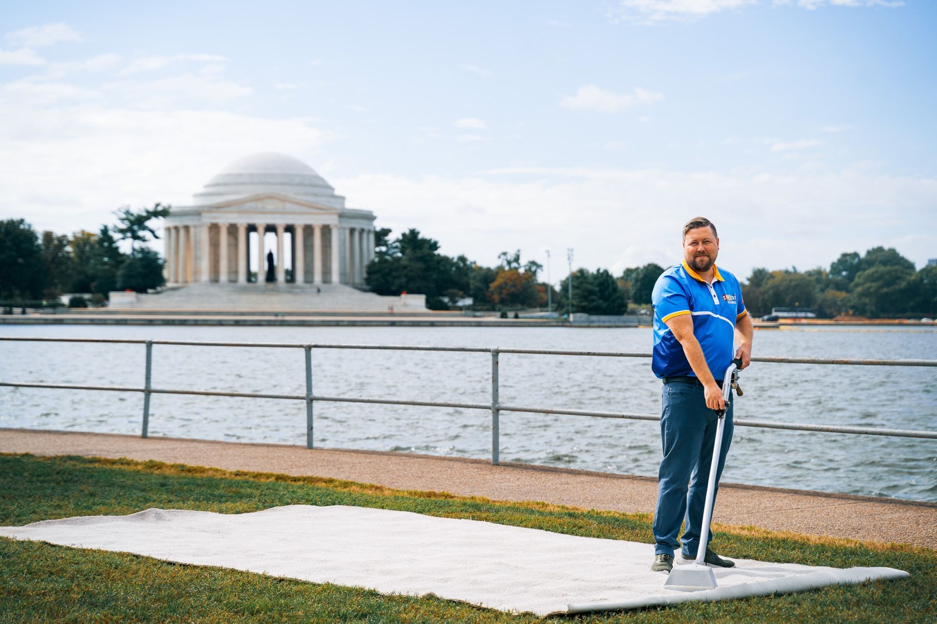 Man stands near the Jefferson Memorial, holding a broom on a light-colored mat.