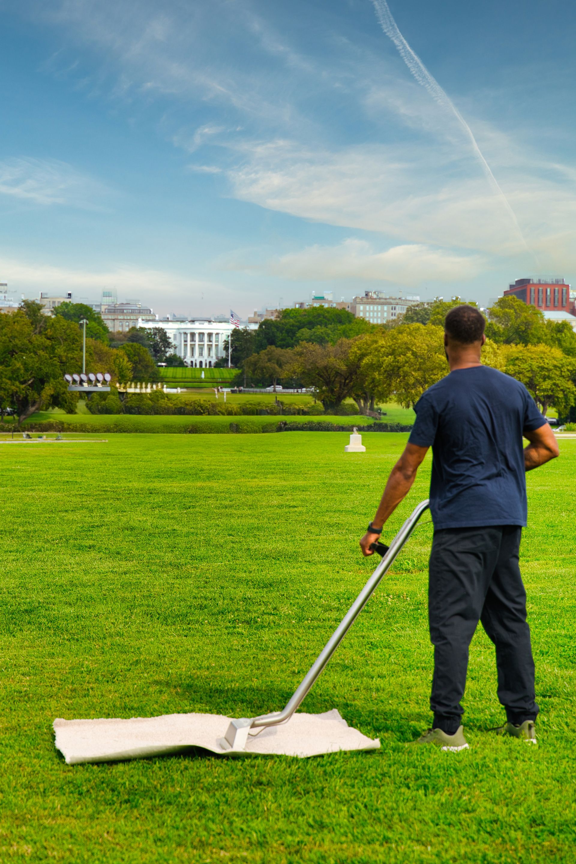 Man using a lawn tool on green grass with the White House in the background under a blue sky.