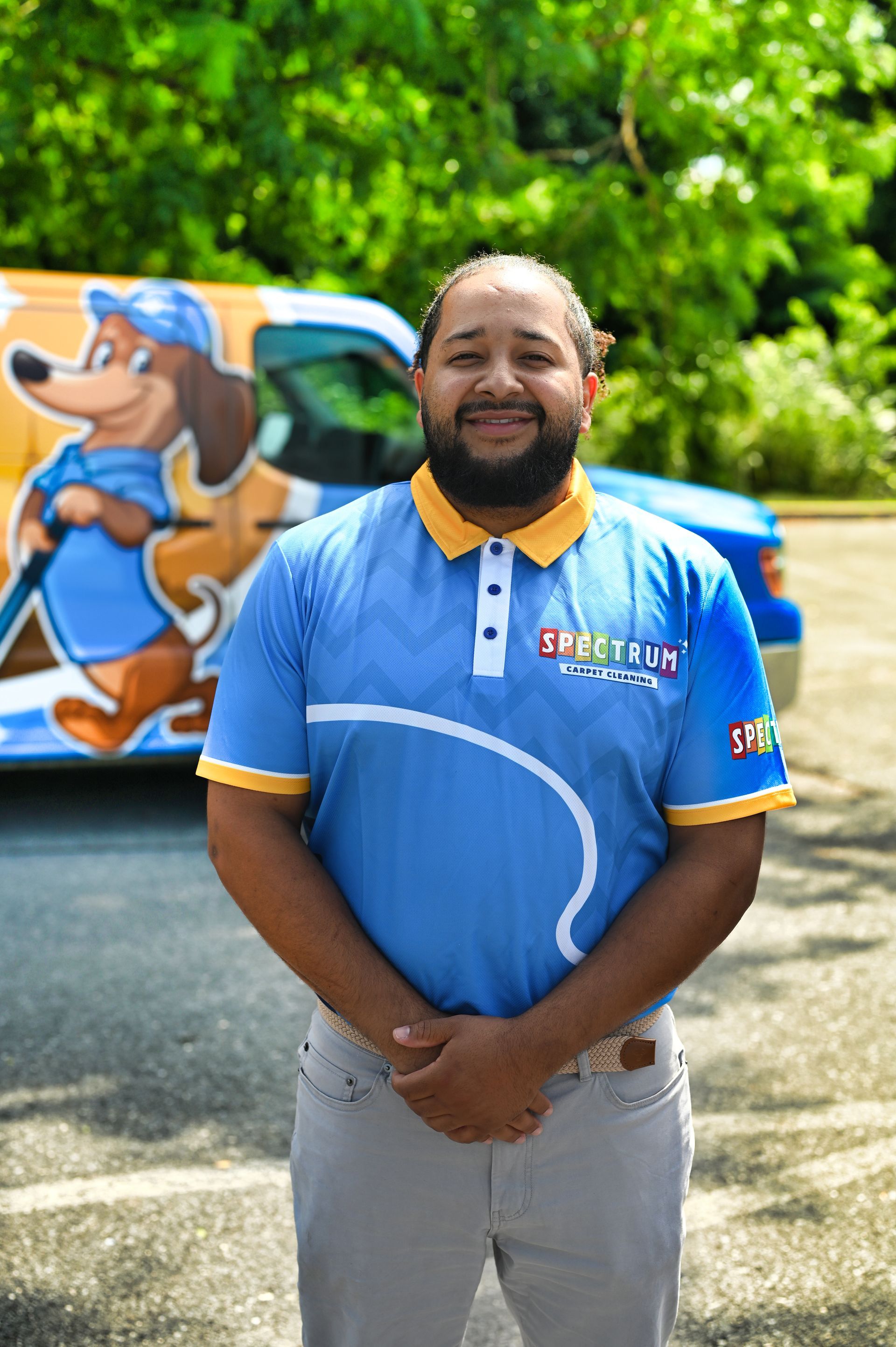 A man with a beard is standing in front of a blue van with his arms crossed.
