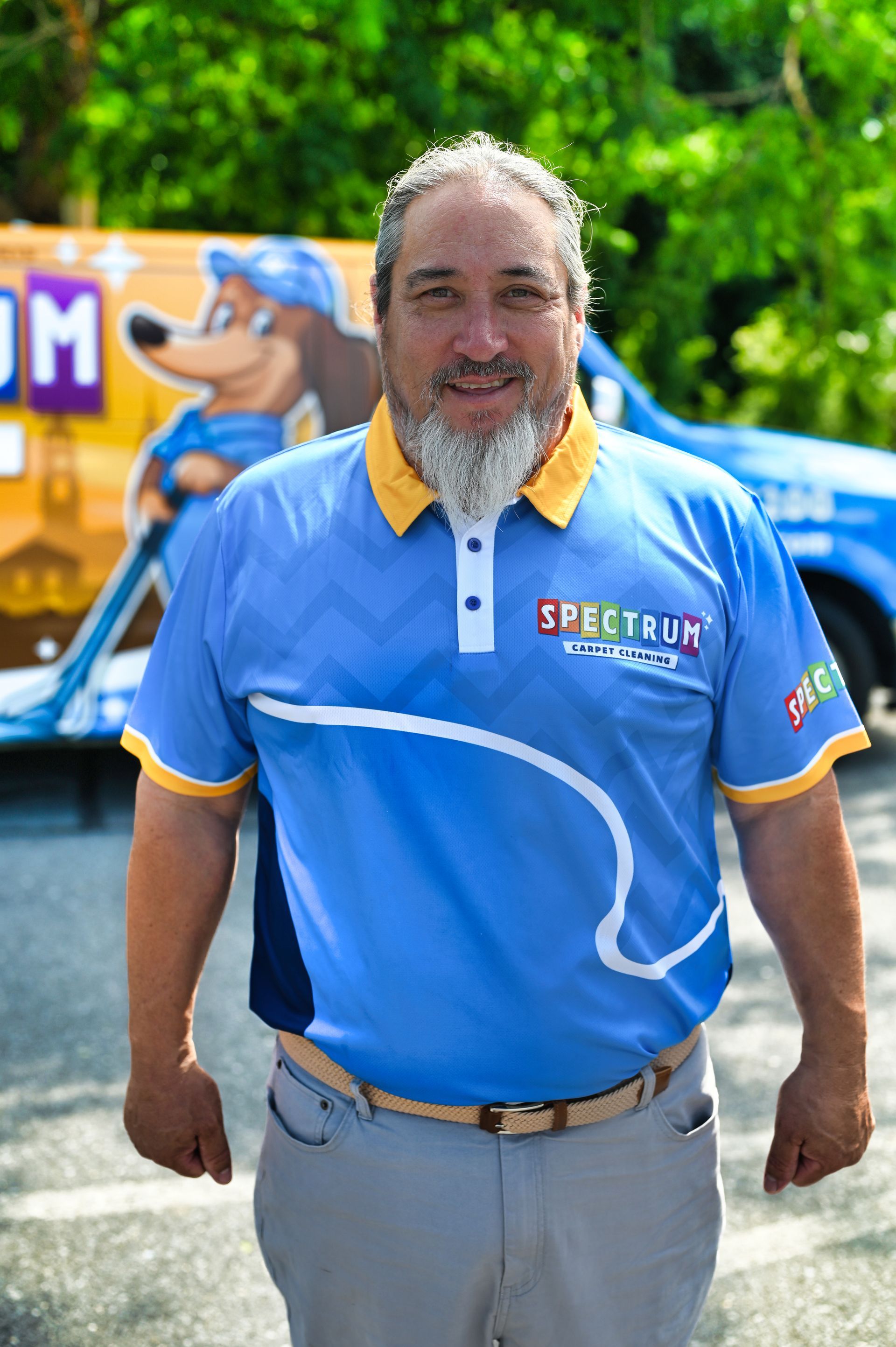A man with a beard is holding a vacuum cleaner and smiling.