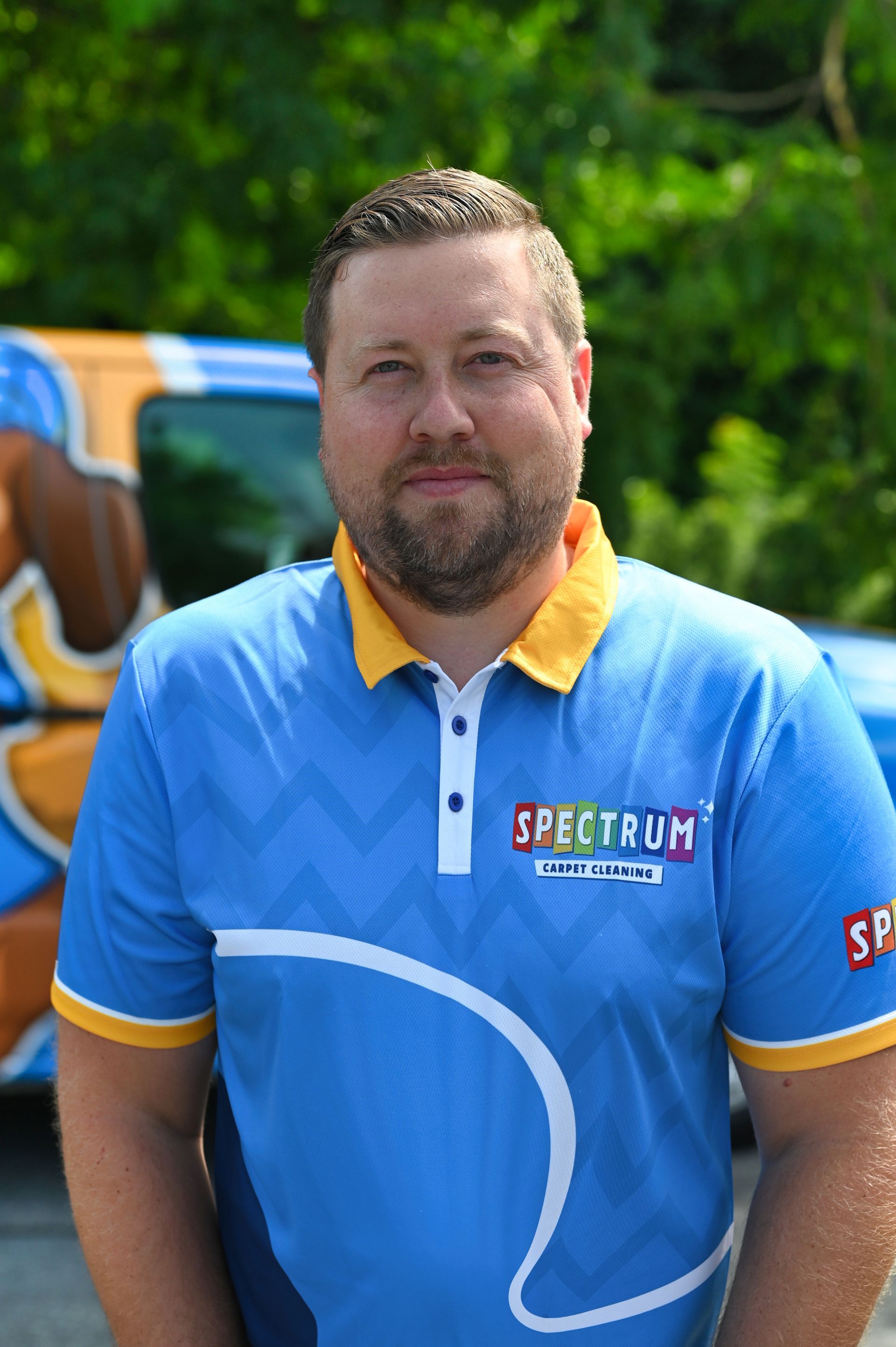 A man in a blue shirt is standing in front of a blue van.