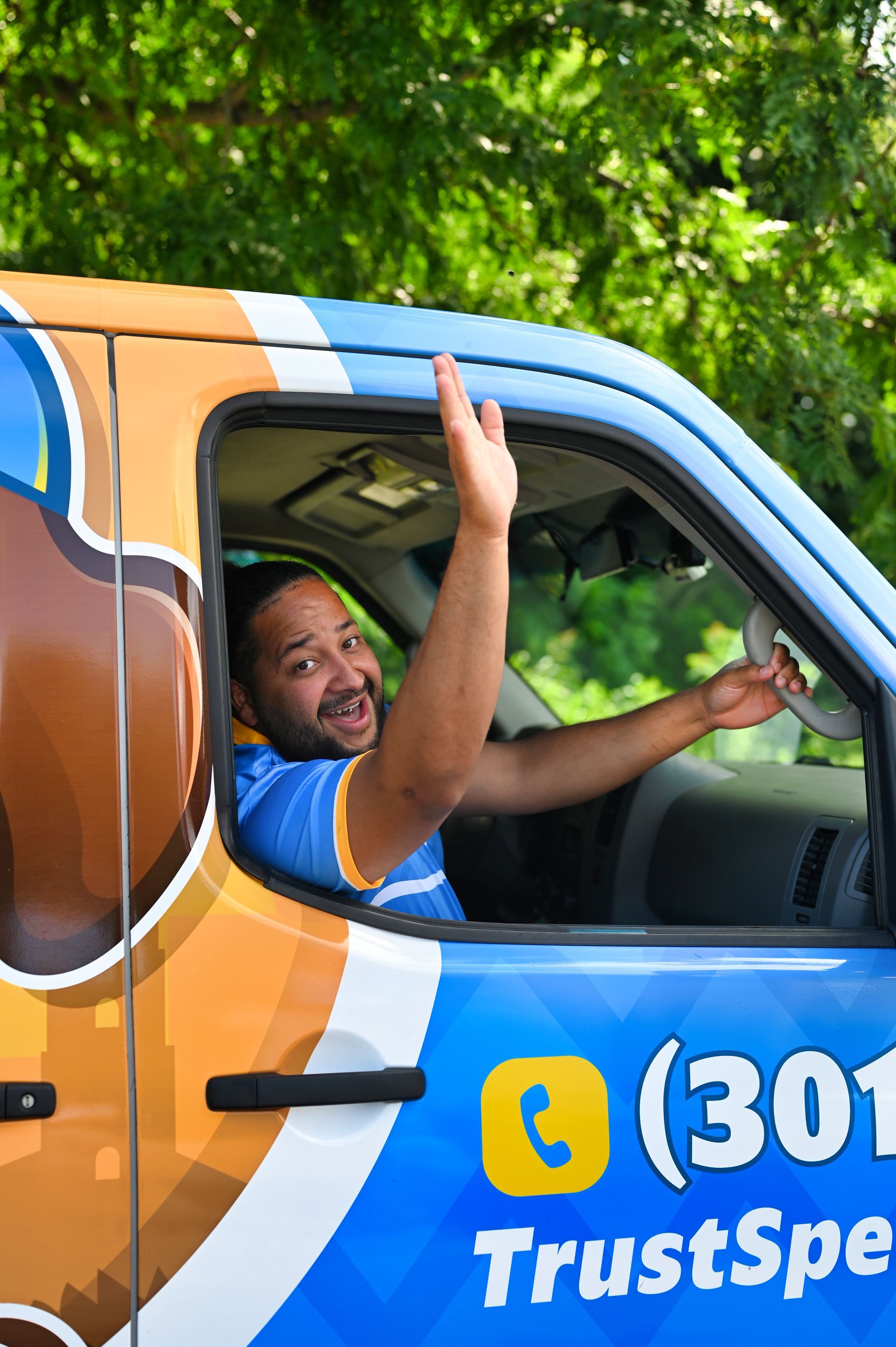 Man waving from a blue and orange company truck, smiling. Phone number and 